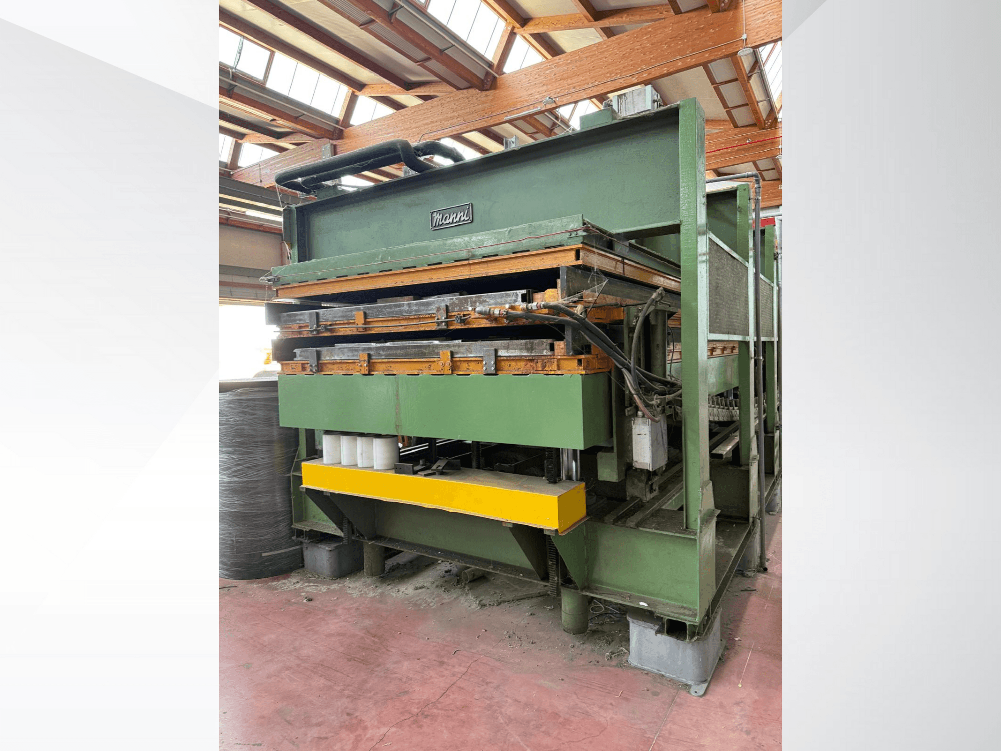 Mannin hydraulinen puristin, sivukuva, jossa vihreä metallirunko, keltainen pohja ja useita hydrauliikkalinjoja näkyvissä.