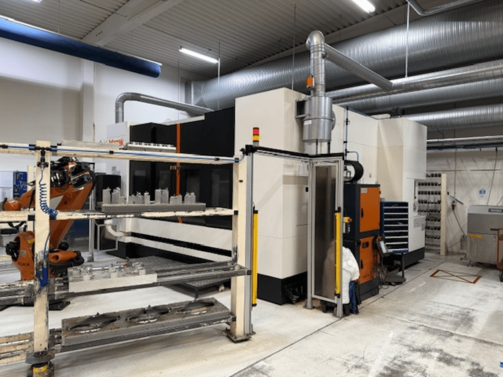 Teollinen CNC-kone, jossa on robottivarsi ja turvakaiteet, ja jossa on etunäkymä asennuksesta ilmavassa työtilassa.