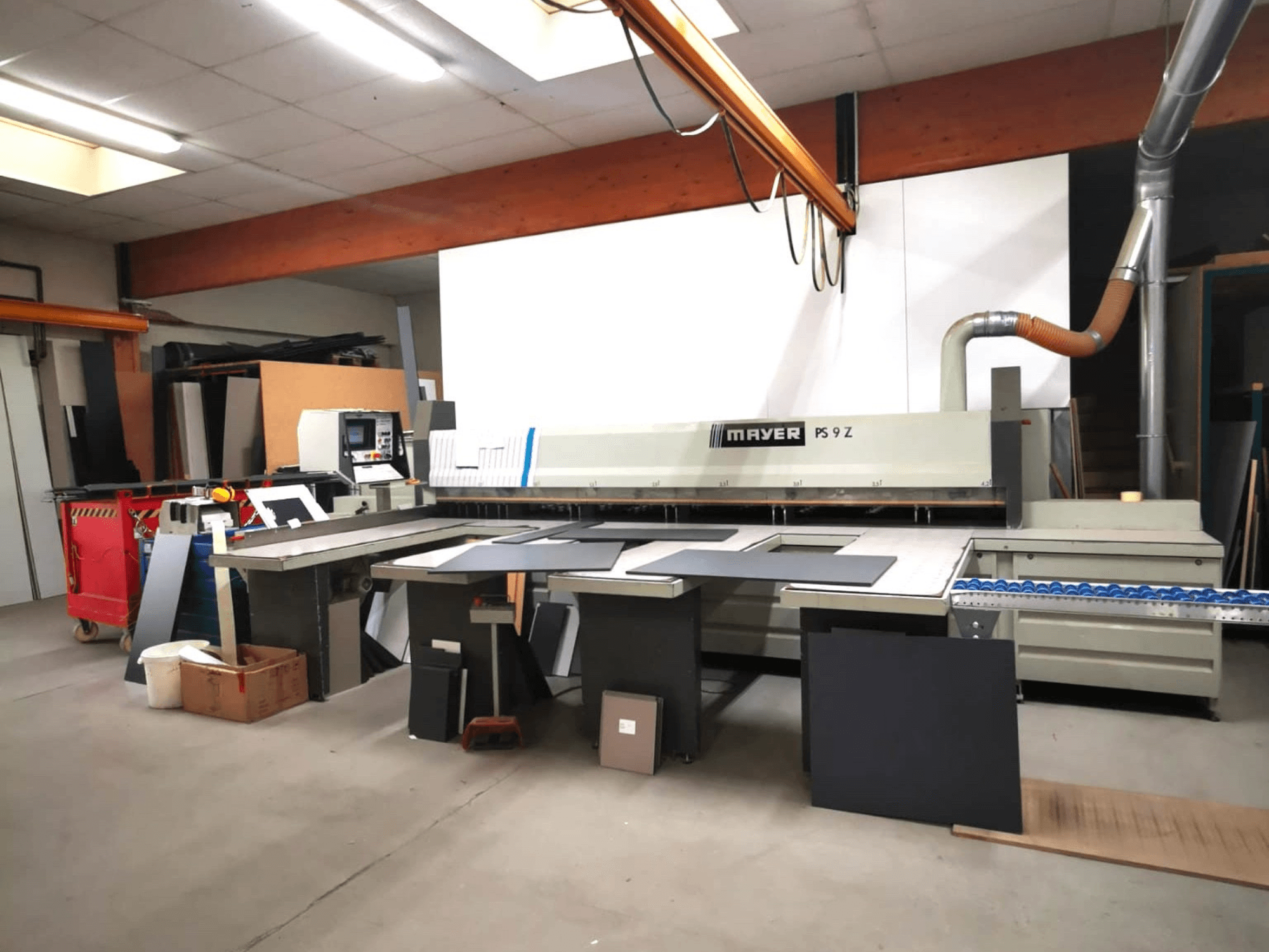 MAYER PS9 Z -leikkauskone työpajassa, etukuva, erilaisia materiaaleja ja kuljetinjärjestelmä näkyvissä.