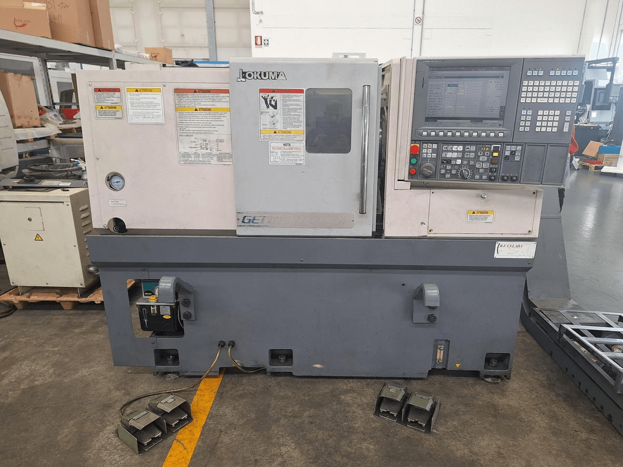 Okuma GENOS L200E-M vaakasuuntainen sorvauskone sivukuvassa; siinä on ohjauspaneeli, turvavaroitukset ja jalkapolkimet.