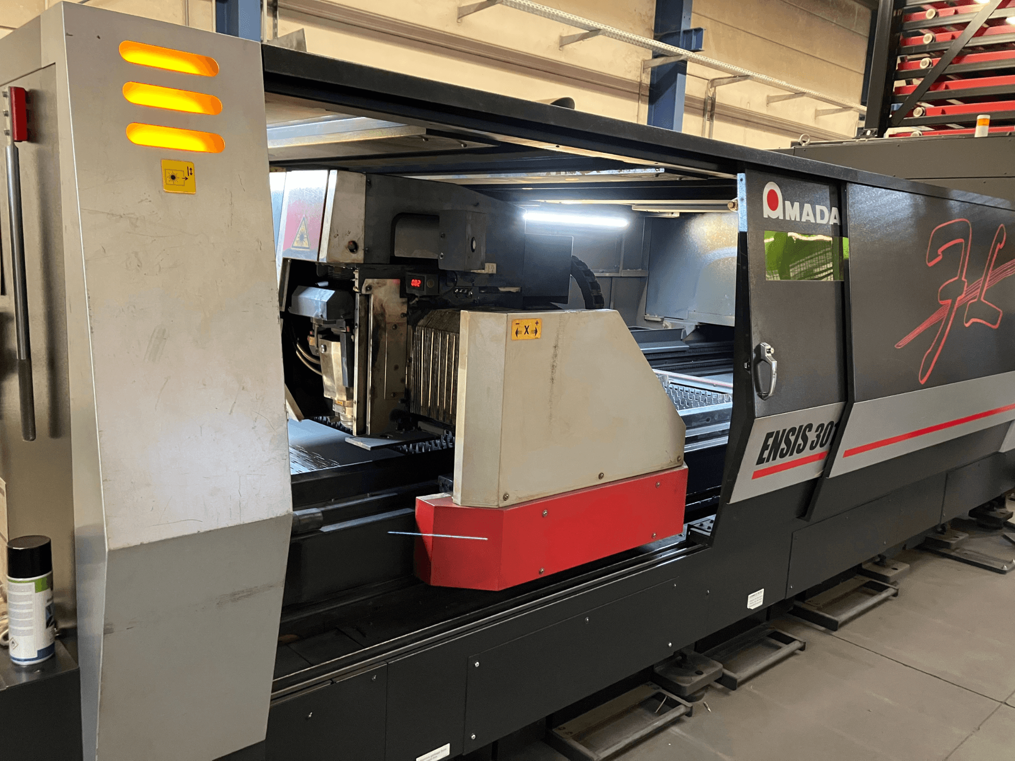 AMADA ENSIS 3015 AJ -kuitulaserleikkauskone, etukuva, jossa leikkauspää ja hallintalaitteet metallisen kehyksen sisällä.