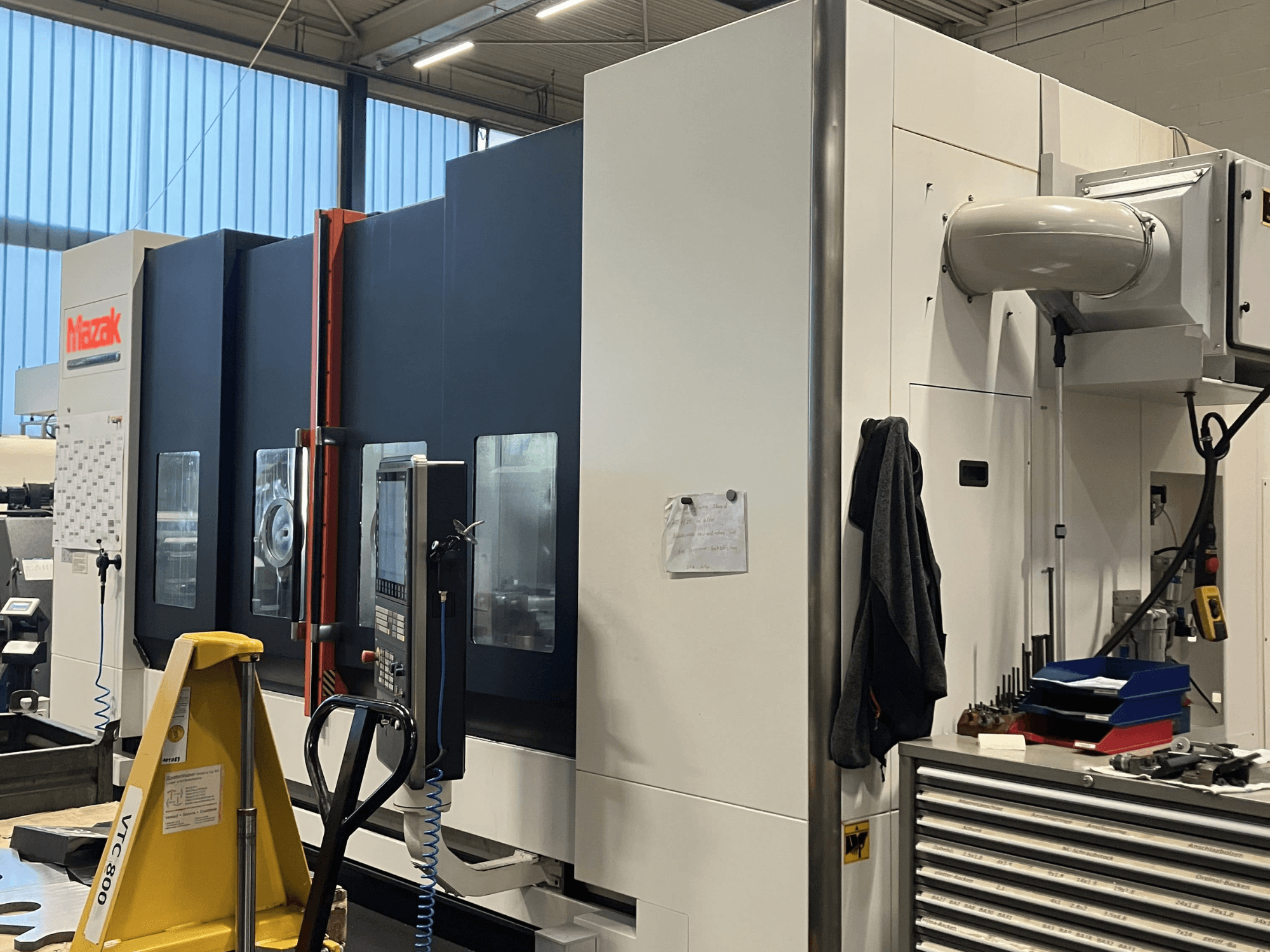 Mazak CNC-kone sivulta katsottuna, jossa näkyy ohjauspaneeli ja turvaominaisuudet työpajassa.