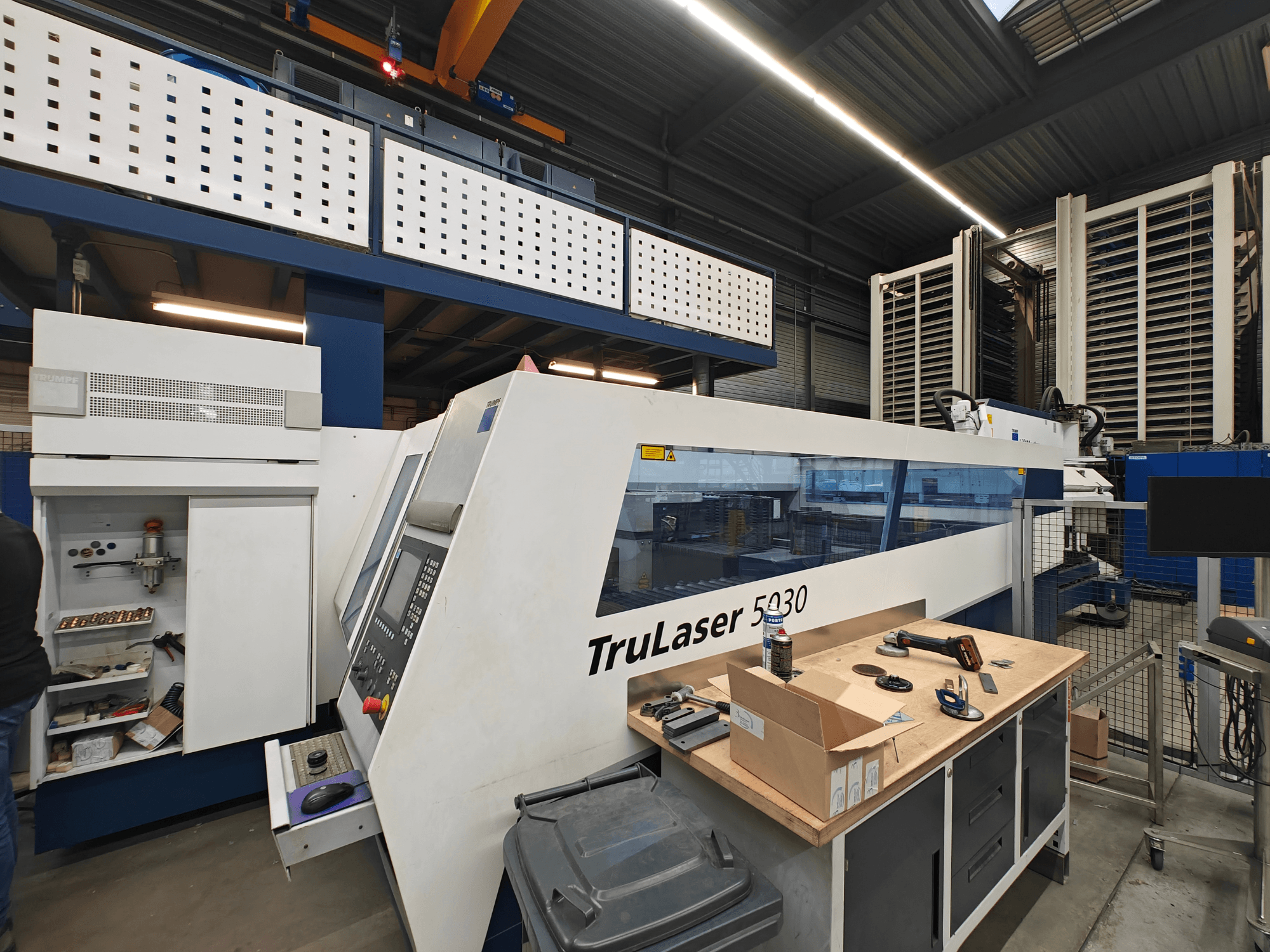 TruLaser 5030 -kone työpajassa, etukuva, jossa ohjauspaneeli näkyvissä, työkalujen ja laitteiden ympäröimänä.