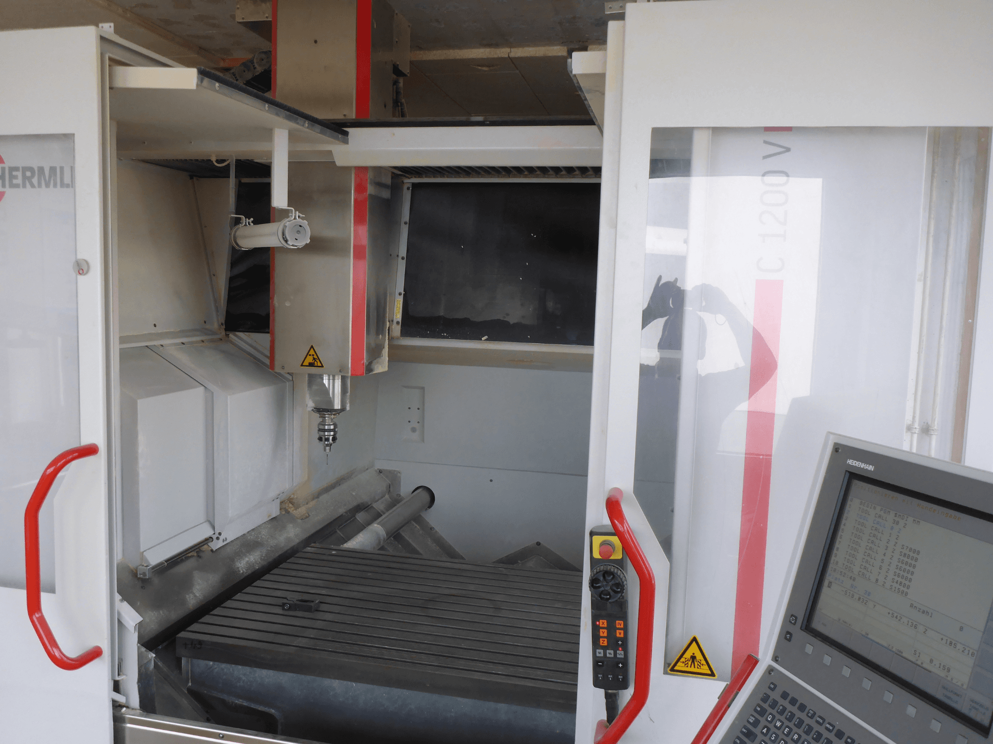 HERMLE C 1200 -pystytyöstökeskuksen sisustus, jossa näkyy työkalunpidin, ohjauspaneeli ja työpöytä edestäpäin.