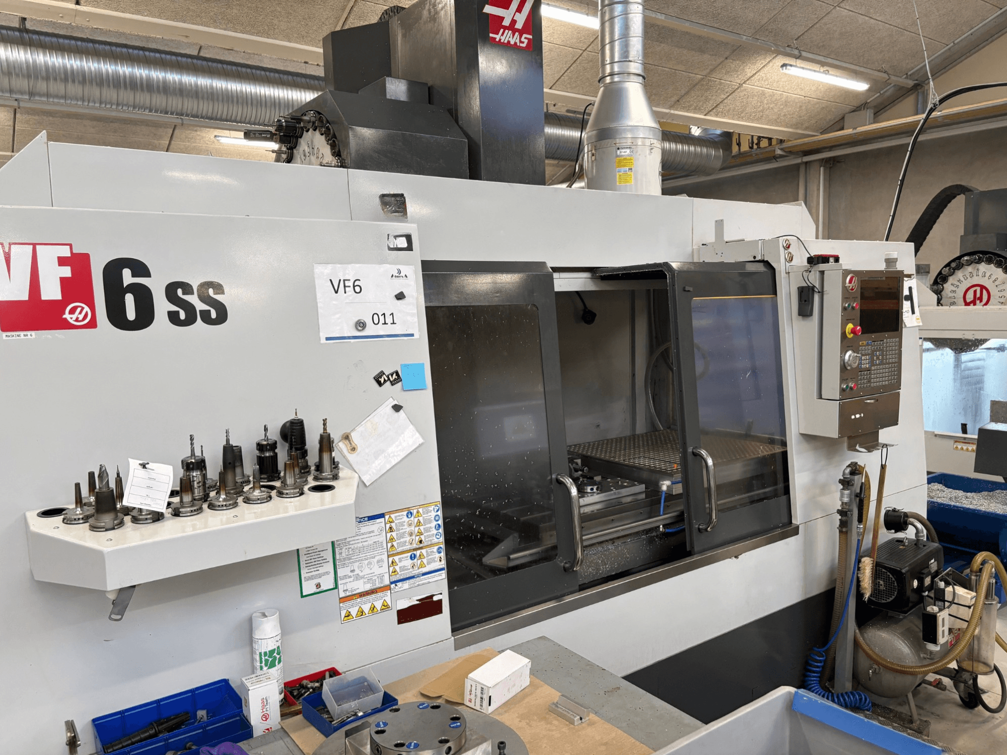 Haas VF-6 SS CNC-jyrsin, etukuva. Erilaisia työkaluja, ohjauspaneeli ja näkyvä sisäinen työtila.