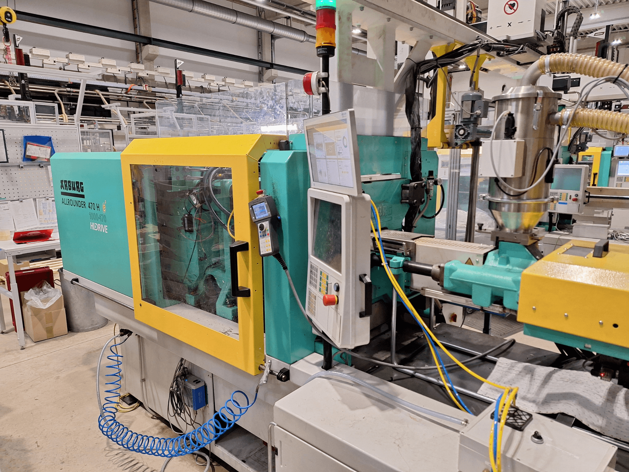 Arburg 470 H 1000-170 hydraulinen ruiskuvalukone, sivukuva ohjauspaneelista ja syöttöjärjestelmästä.