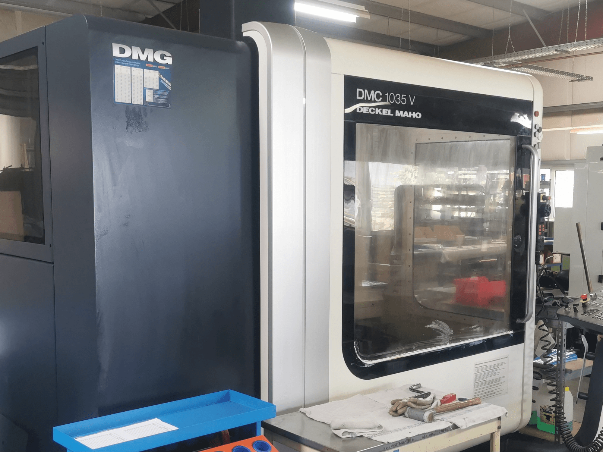DMG DMC 1035 V -jyrsinkone työpajassa, etukuva, sininen työkalulokero ja käsineet pinnalla.