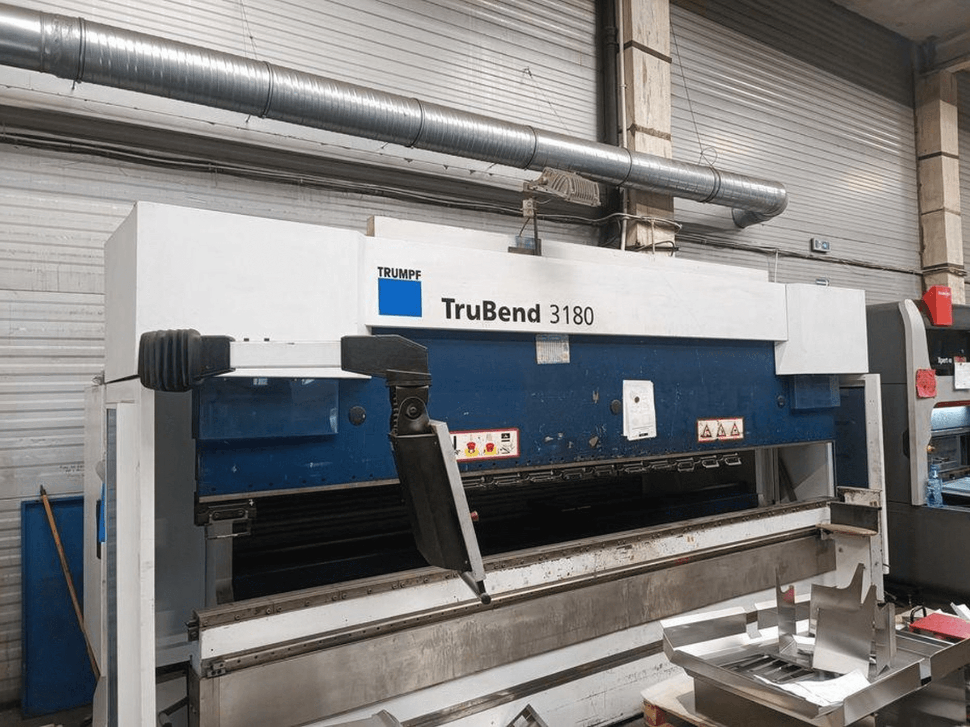 Trumpf TruBend 3180 -taivutuskone työpajassa, sivukuva, jossa näkyy ohjauspaneeli ja metallikappaleet pöydällä.