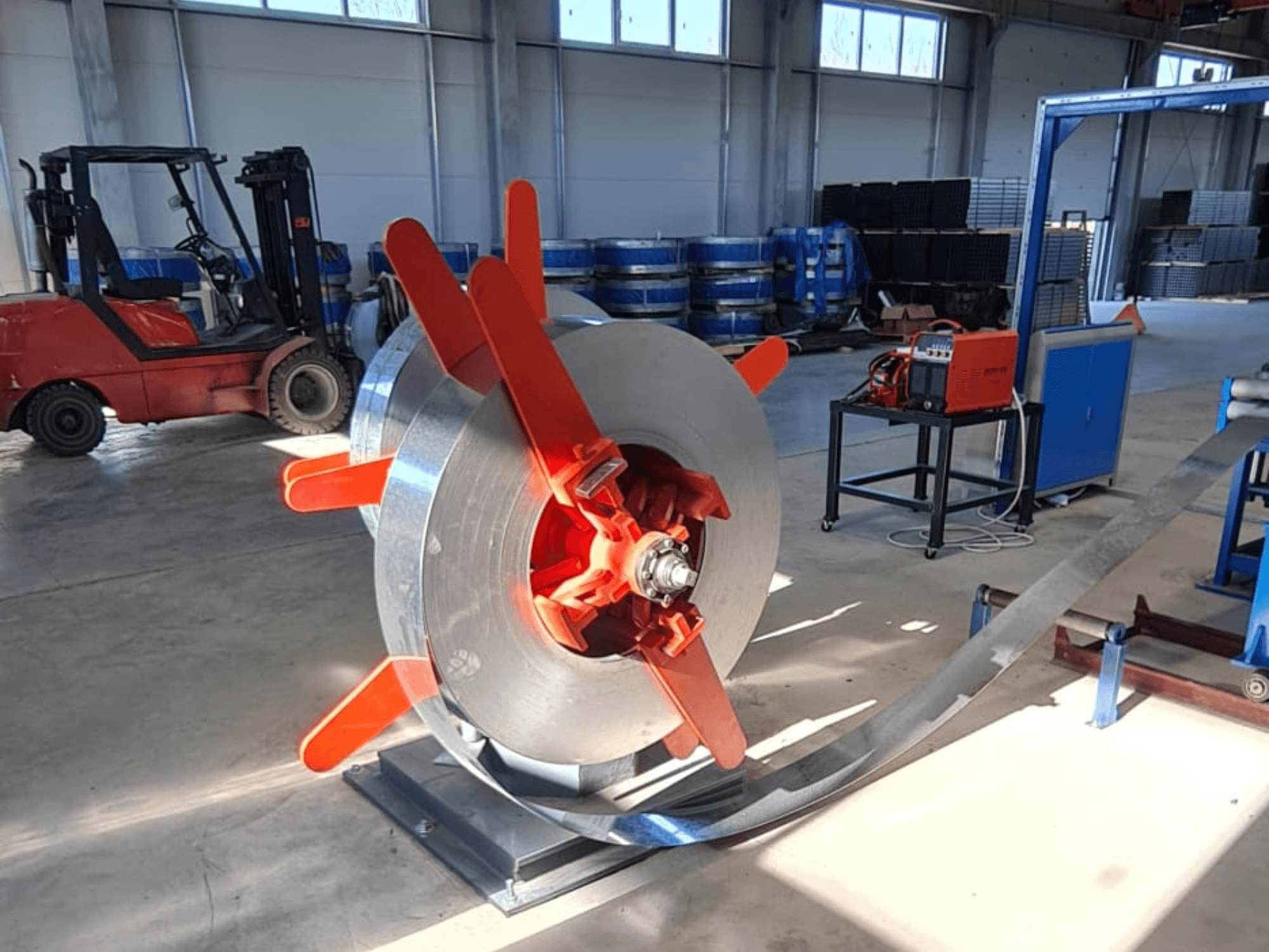 Punaisilla kahvoilla varustettu metallikela jalustalla, kuvakulmasta katsottuna. Teollinen tausta, jossa on koneita ja trukki.