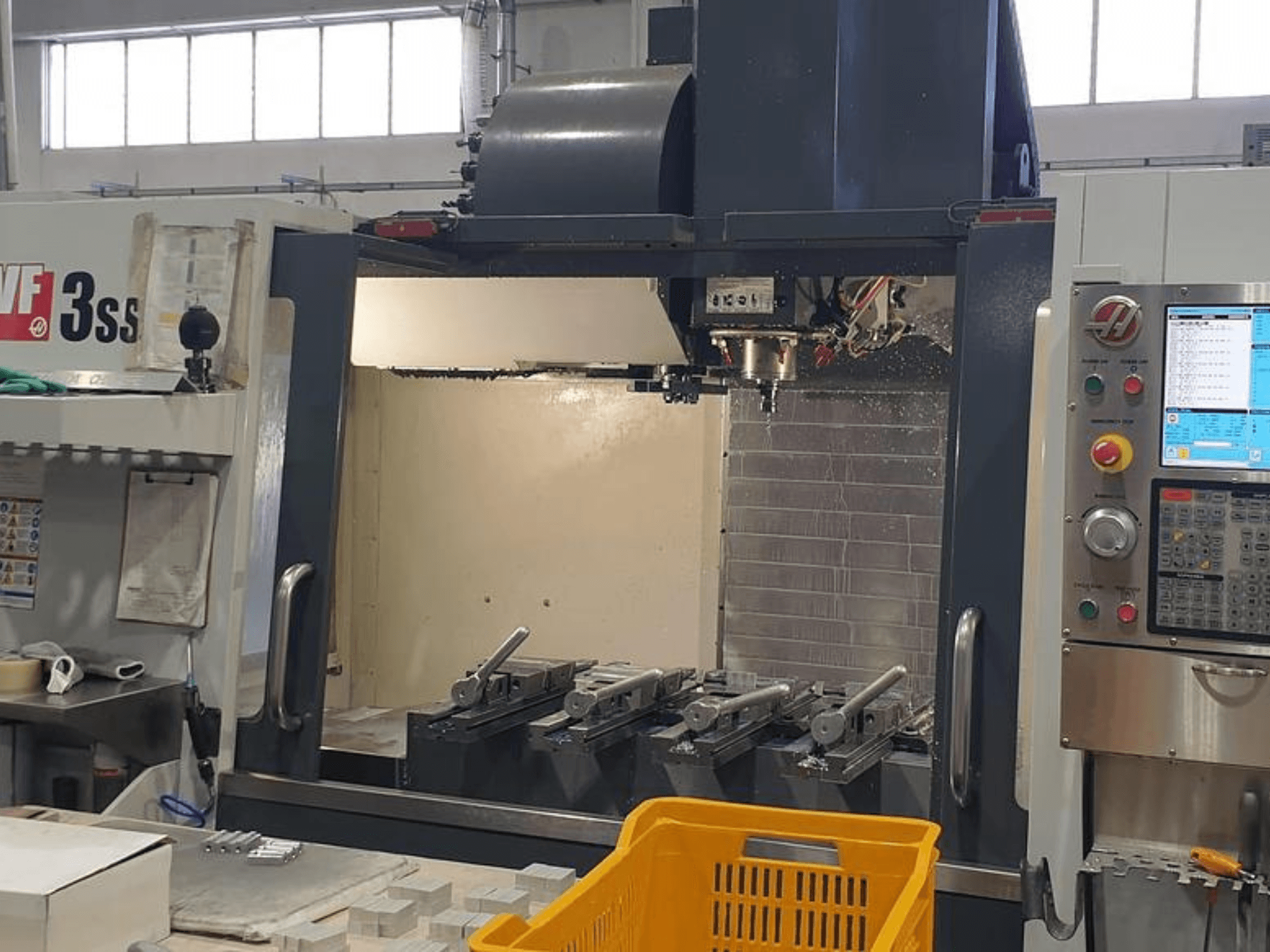 HAAS VF-3SS -pystytyöstökeskus, etukuva, jossa CNC-ohjauspaneeli, työkalut ja oranssi kori.
