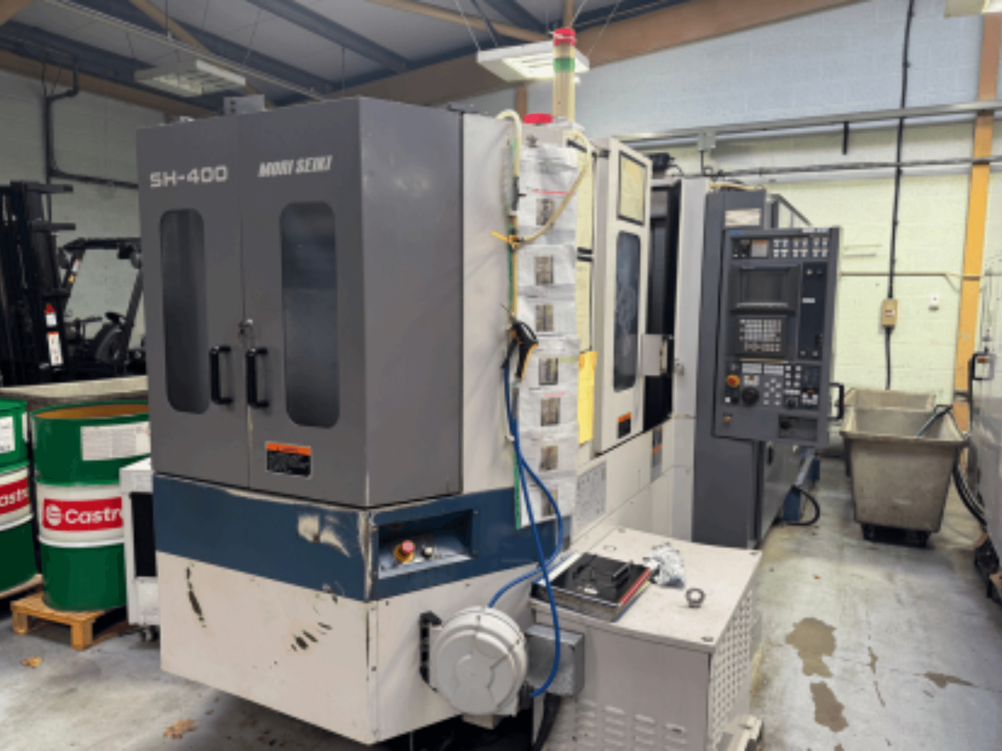 Moni Seiki SH-400 CNC-kone, sivukuva, jossa näkyy ohjauspaneeli, ovet ja ympäröivä teollisuusympäristö.