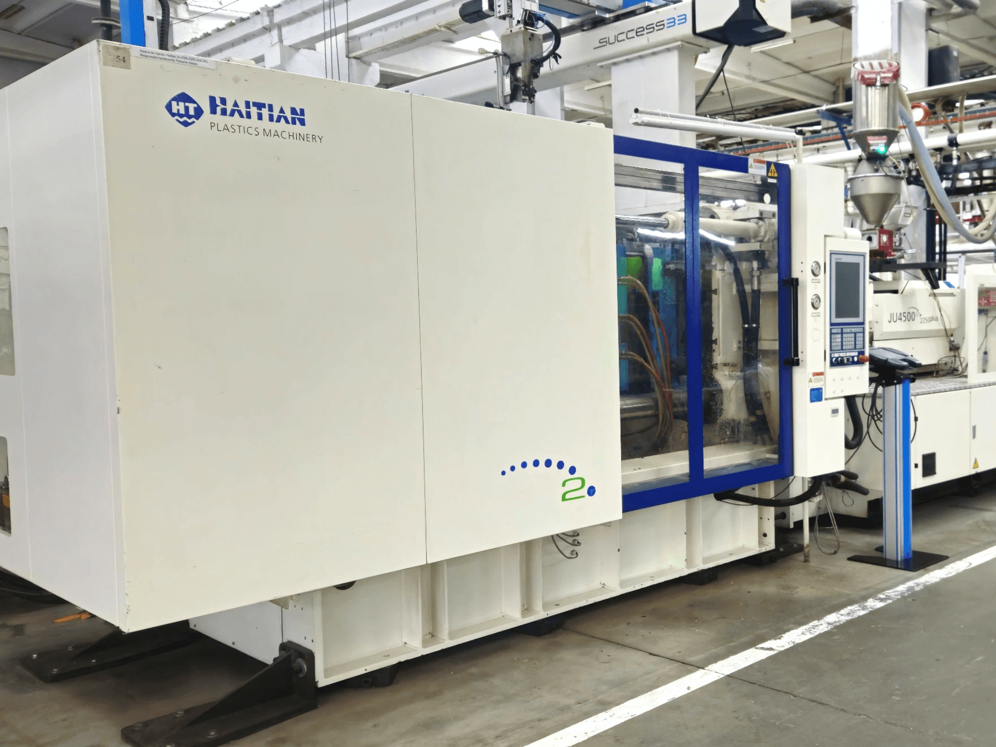 Haitian Plastics Machinery -malli, etukuva, jossa esitellään kone, jossa on ohjauspaneeli ja näkyvät letkut, teollisuusympäristössä.