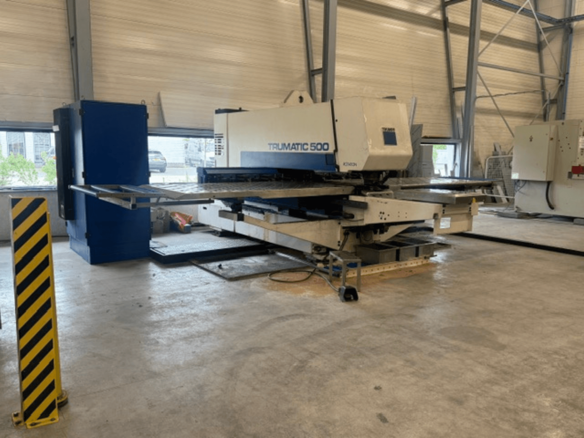 CNC-lävistyskone TRUMPF Trumatic 500 työpajassa, sivukuva, jossa näkyy kone ja keltaisilla raidoilla varustettu turvapylväs.