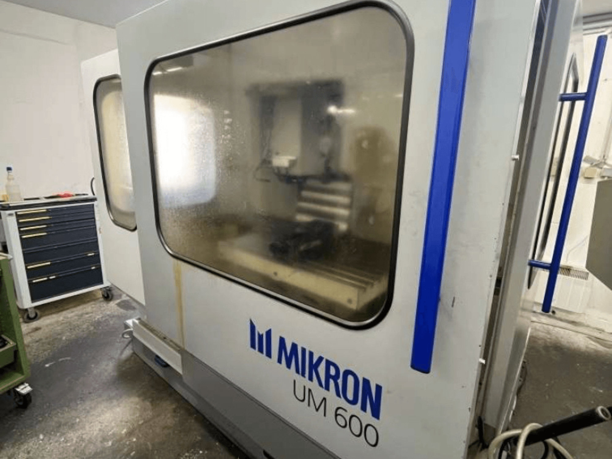 MIKRON UM 600 TNC 410/426 yleiskoneistuskeskus, sivukuva, jossa on huurtunut lasi ja näkyvissä oleva työkalujen säilytys lähellä.