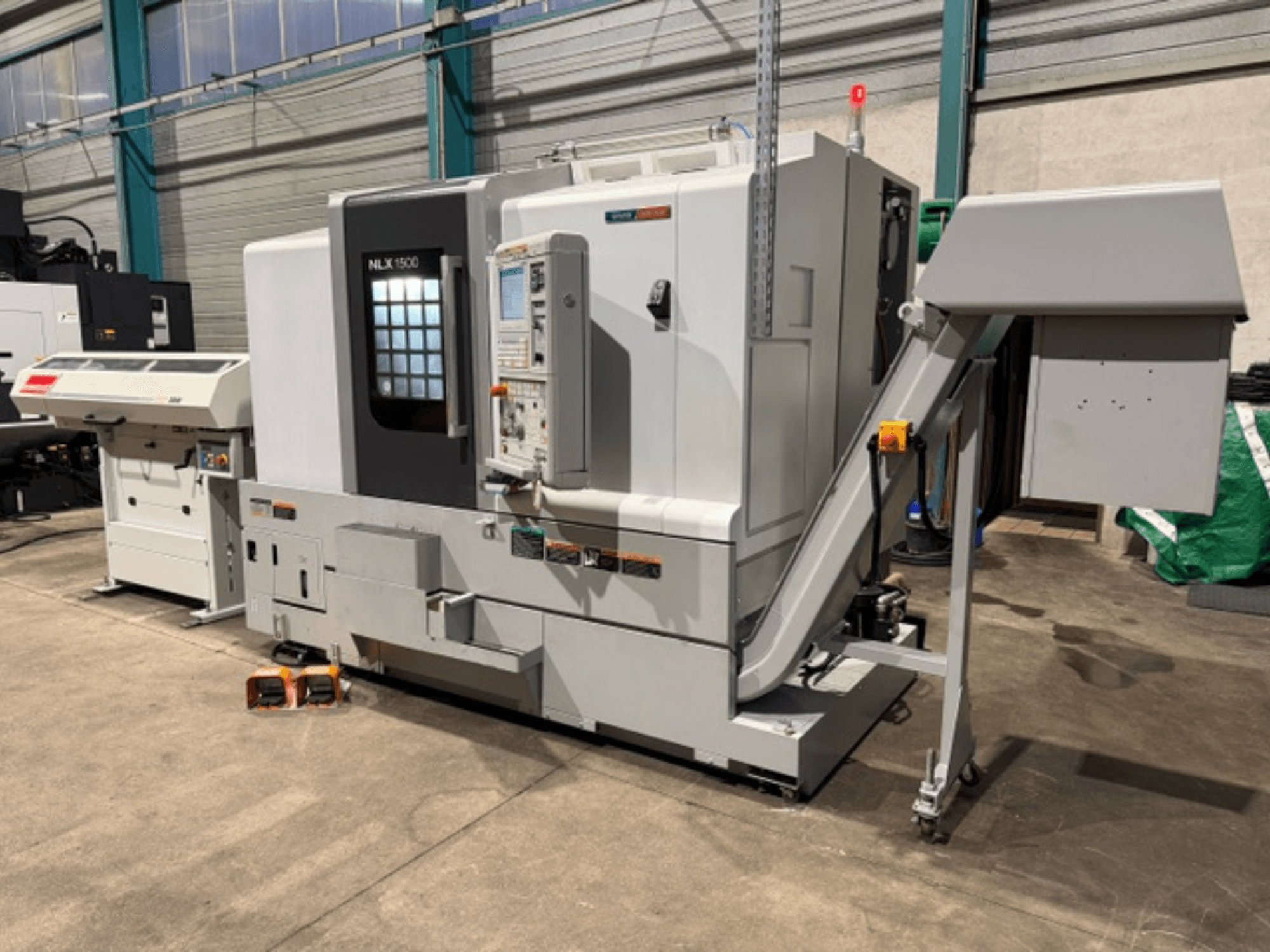 NLK 1500 CNC-kone, etukuva, ohjauspaneeli ja tarvikesäiliö sivulla, betonilattialla.