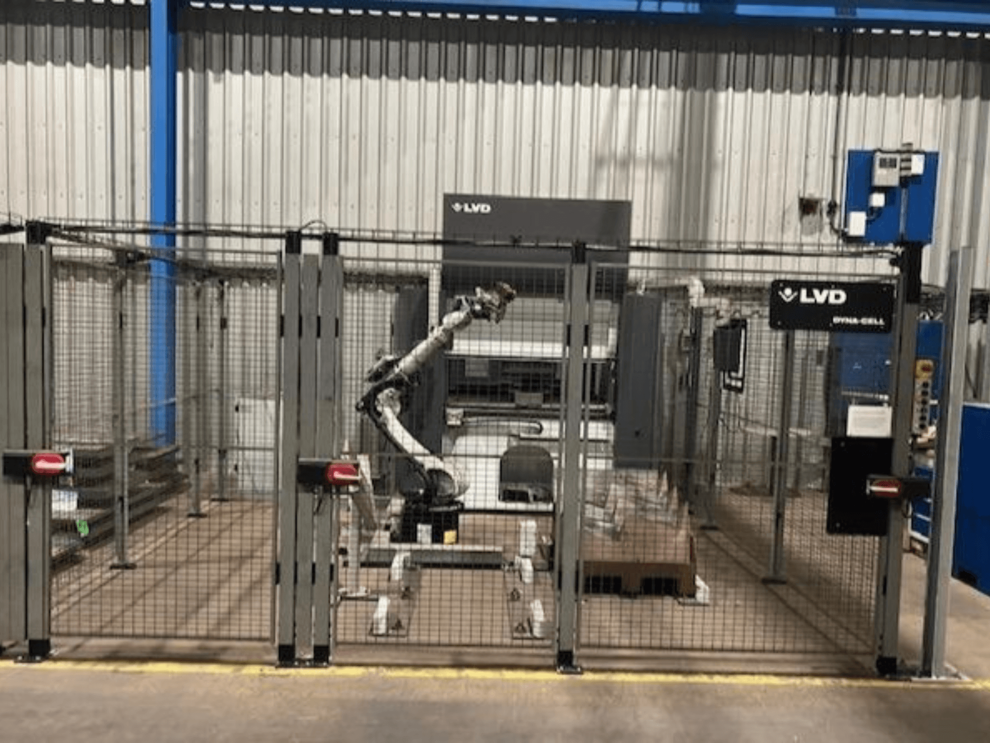 LVD Dyna-Cell -robottityöasema aidatussa kotelossa, etukuva, jossa robottivarsi ja ohjauspaneeli.