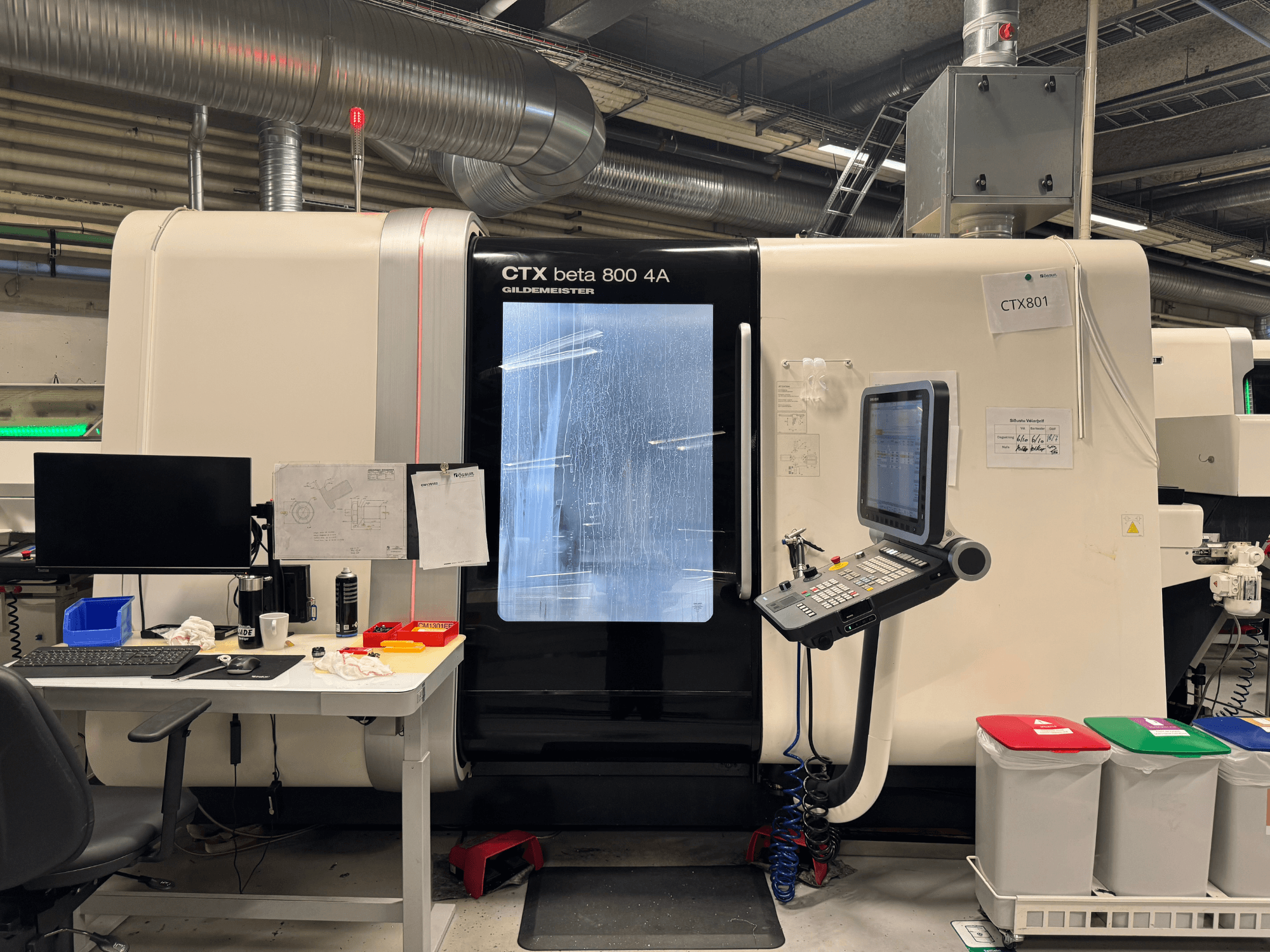 CTX beta 800 4A -kone ohjauspaneelilla ja monitorilla, sivukuva, työpajassa, jossa on toimisto ja värillisiä roskakoreja.