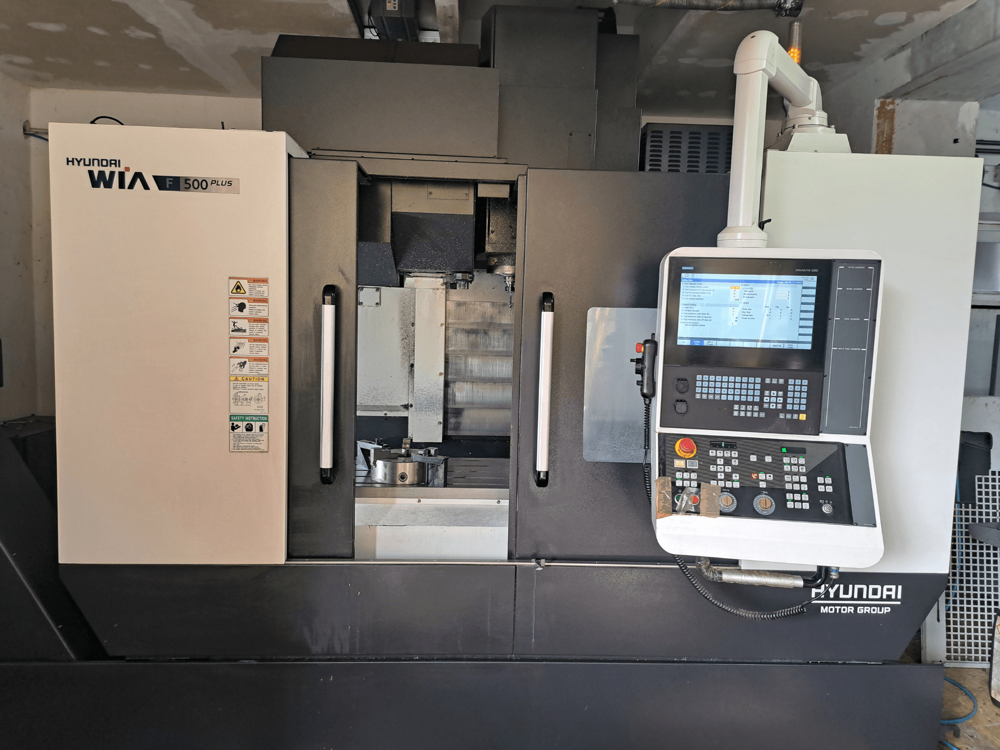 Hyundai WIA F500 Plus CNC-kone etukuvassa, jossa on digitaalinen ohjauspaneeli ja turvatarrat.