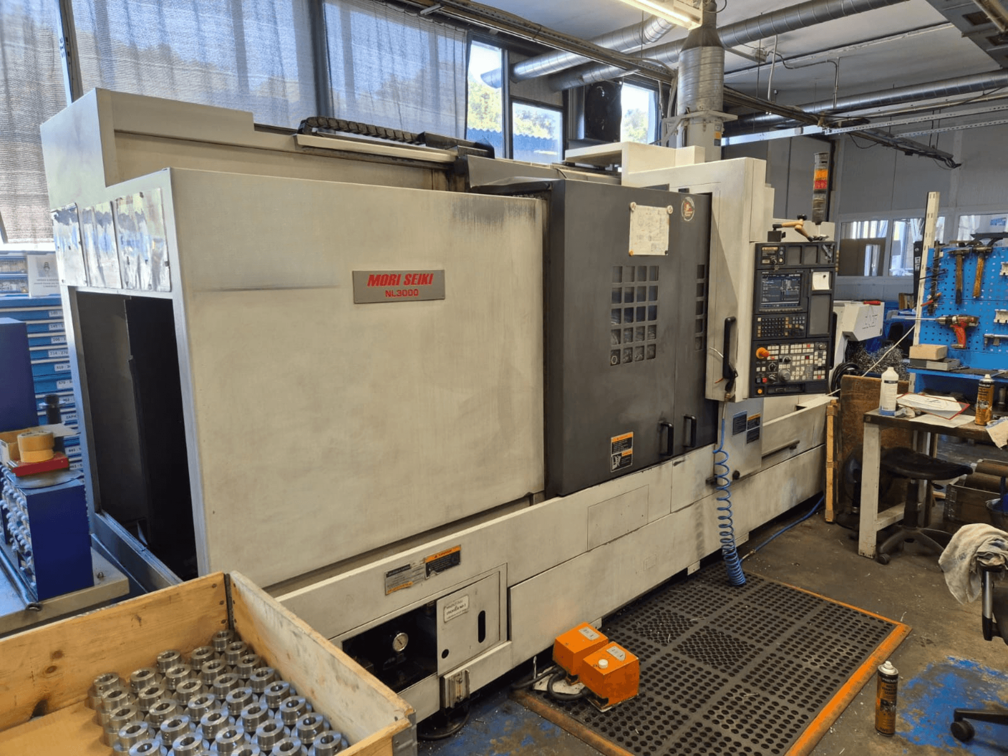 Mori Seiki NL3000 CNC-sorvi työpajassa, sivukuva ohjauspaneelista, työkaluista ja metalliosista puulaatikossa.
