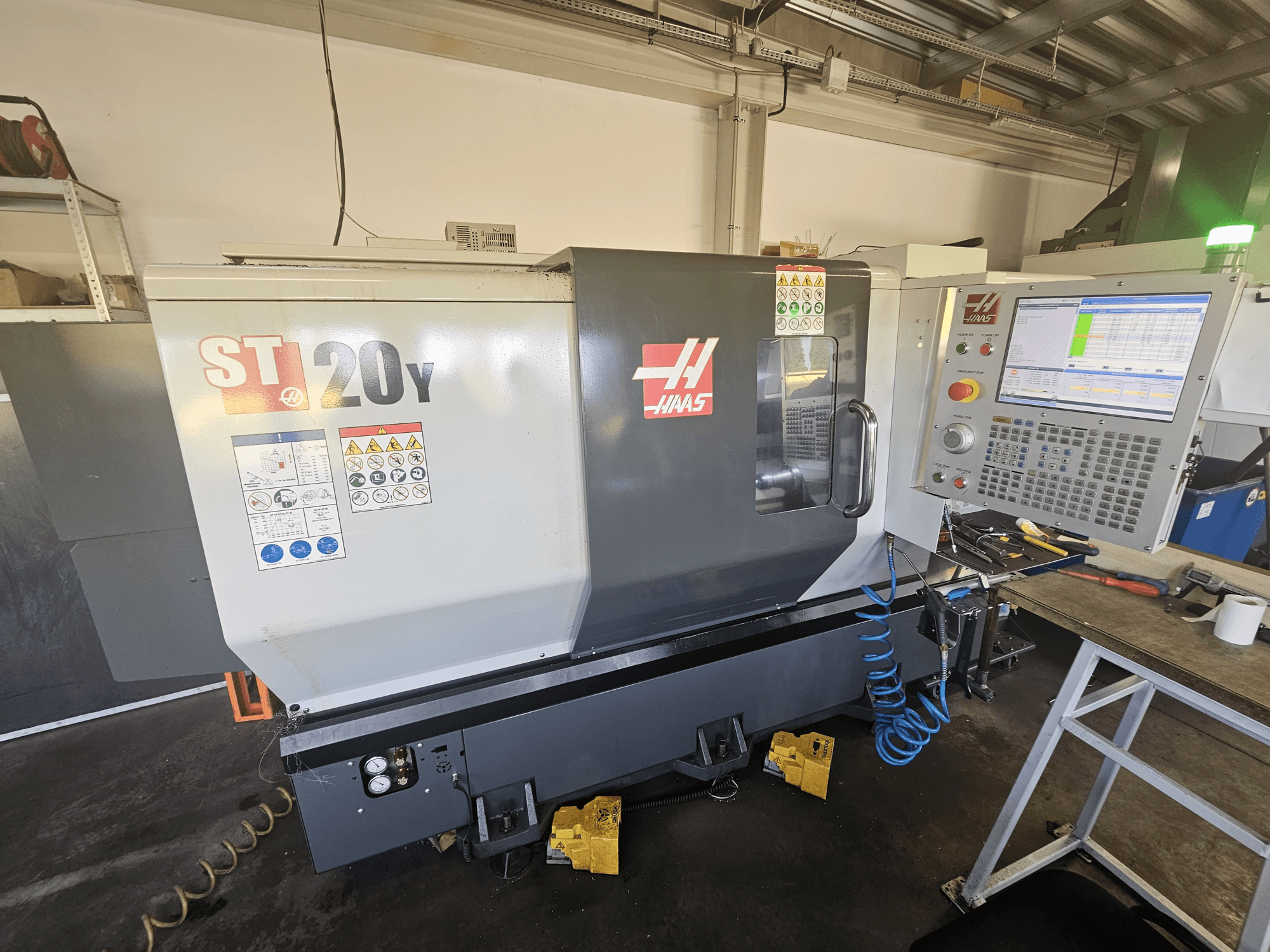Haas ST-20Y CNC-sorvi edestä ja ohjauspaneeli; sisältää turvatarrat ja ilmaletkun yksityiskohdat sivulla.