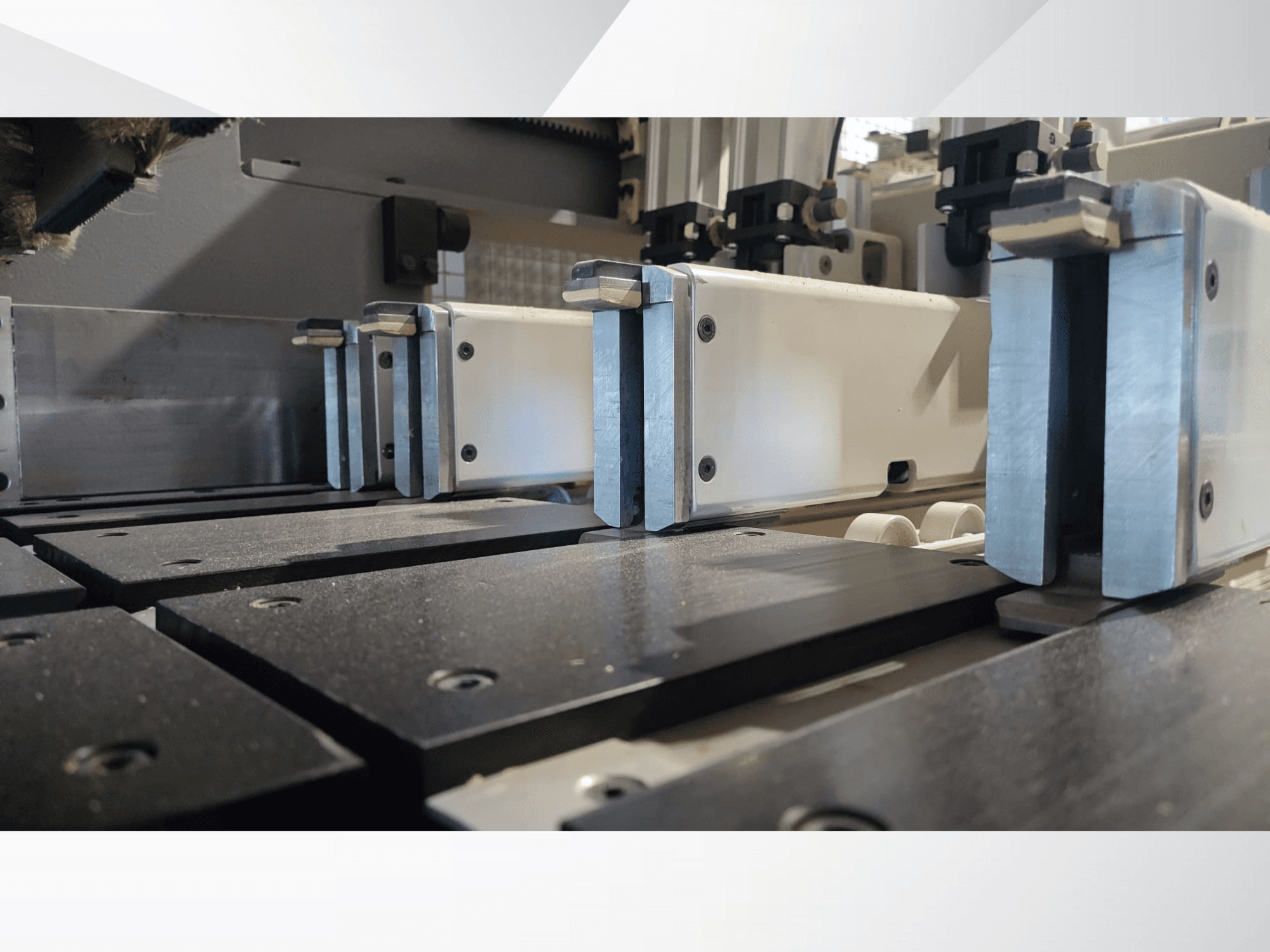 Lähikuva tarkkuuskoneen metallisilla leuoilla varustetusta kiinnitysmekanismista, jossa on mustat työpinnat ja näkyvät ohjainkiskot.