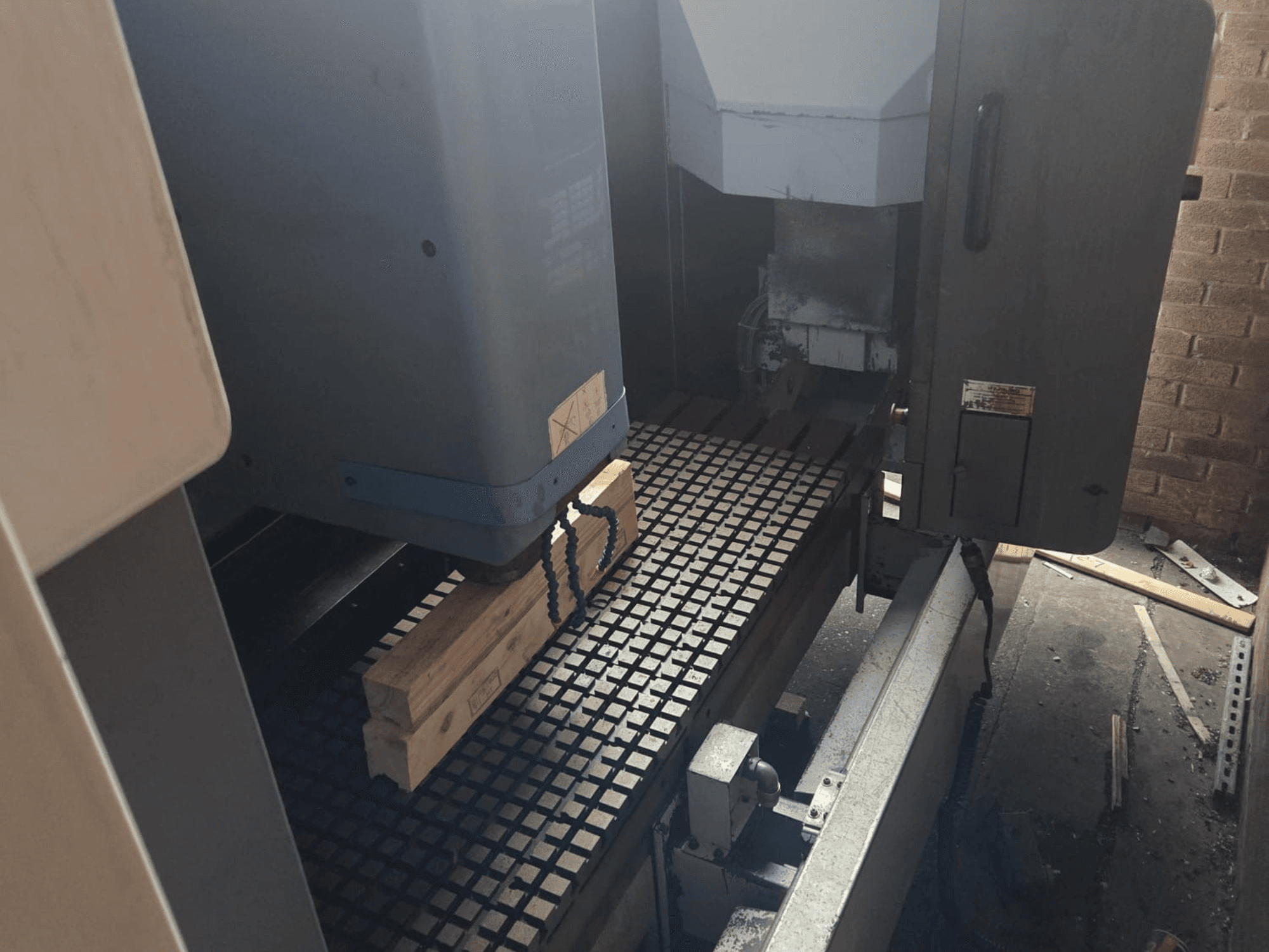 CNC-koneen etunäkymä, jossa on puulankkuja ristikkopöydällä, työkalut ja hallintalaitteet sivulla.