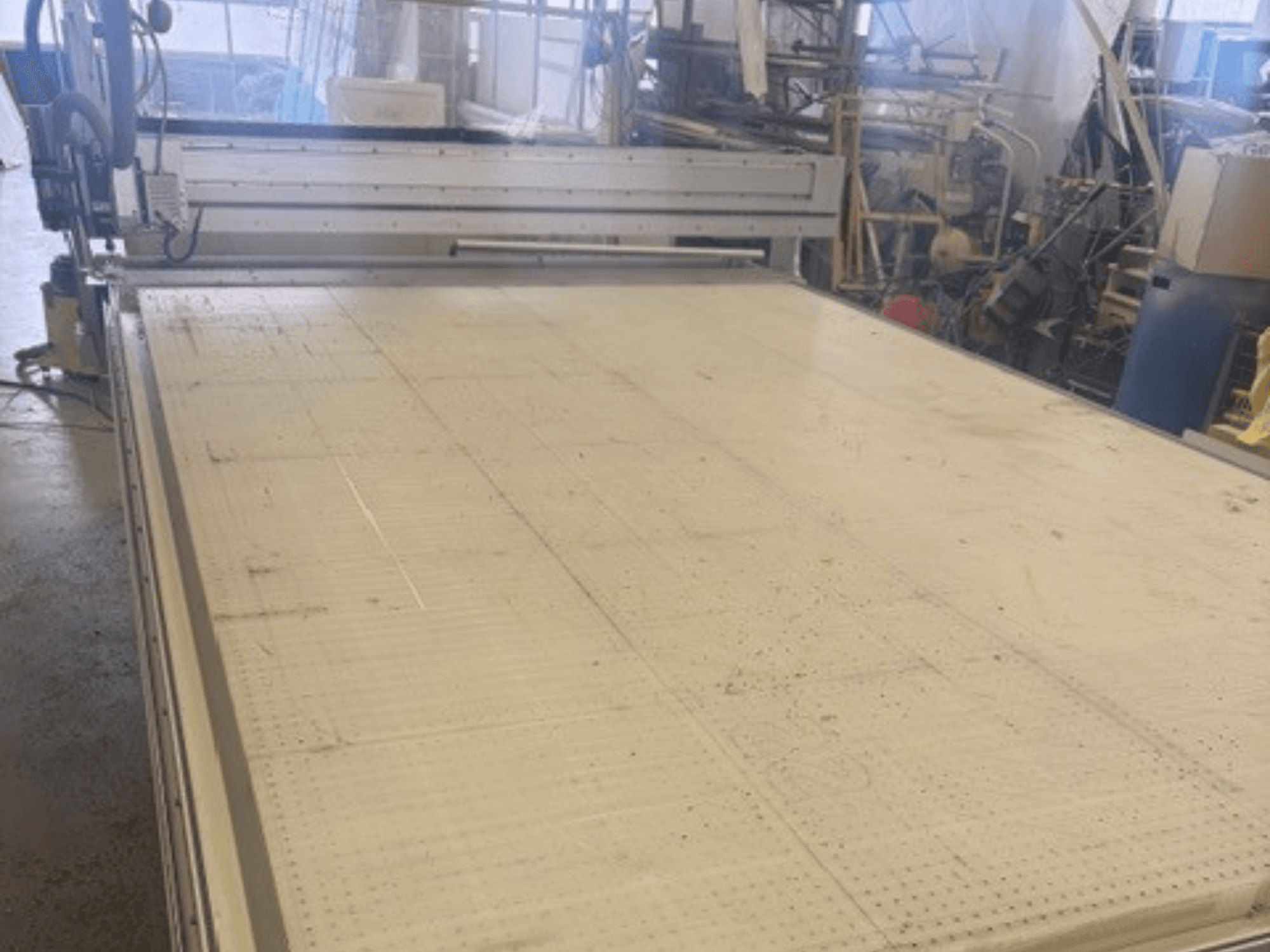 Suuri leikkuukone, jossa on tasainen pinta, jossa näkyy runko ja ohjainkisko; kuvattu kulmasta työpajassa.