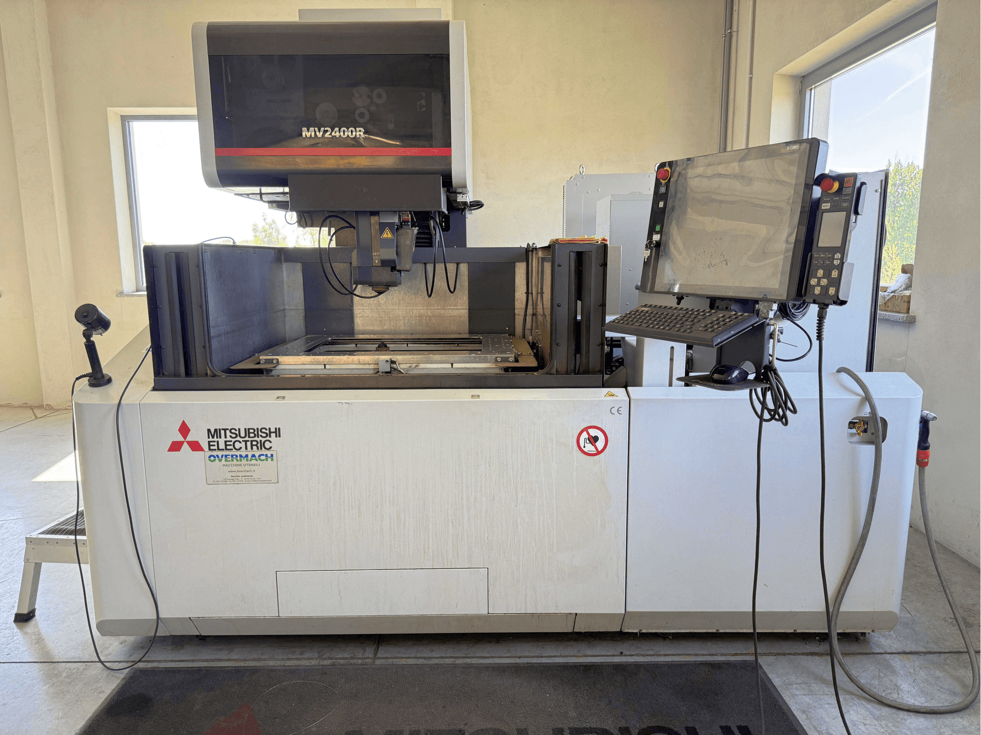 Mitsubishi MV2400R -lankasähköleikkauskone edestä katsottuna; kuvassa näkyvät ohjauspaneeli, työtila ja turvallisuusmerkinnät.