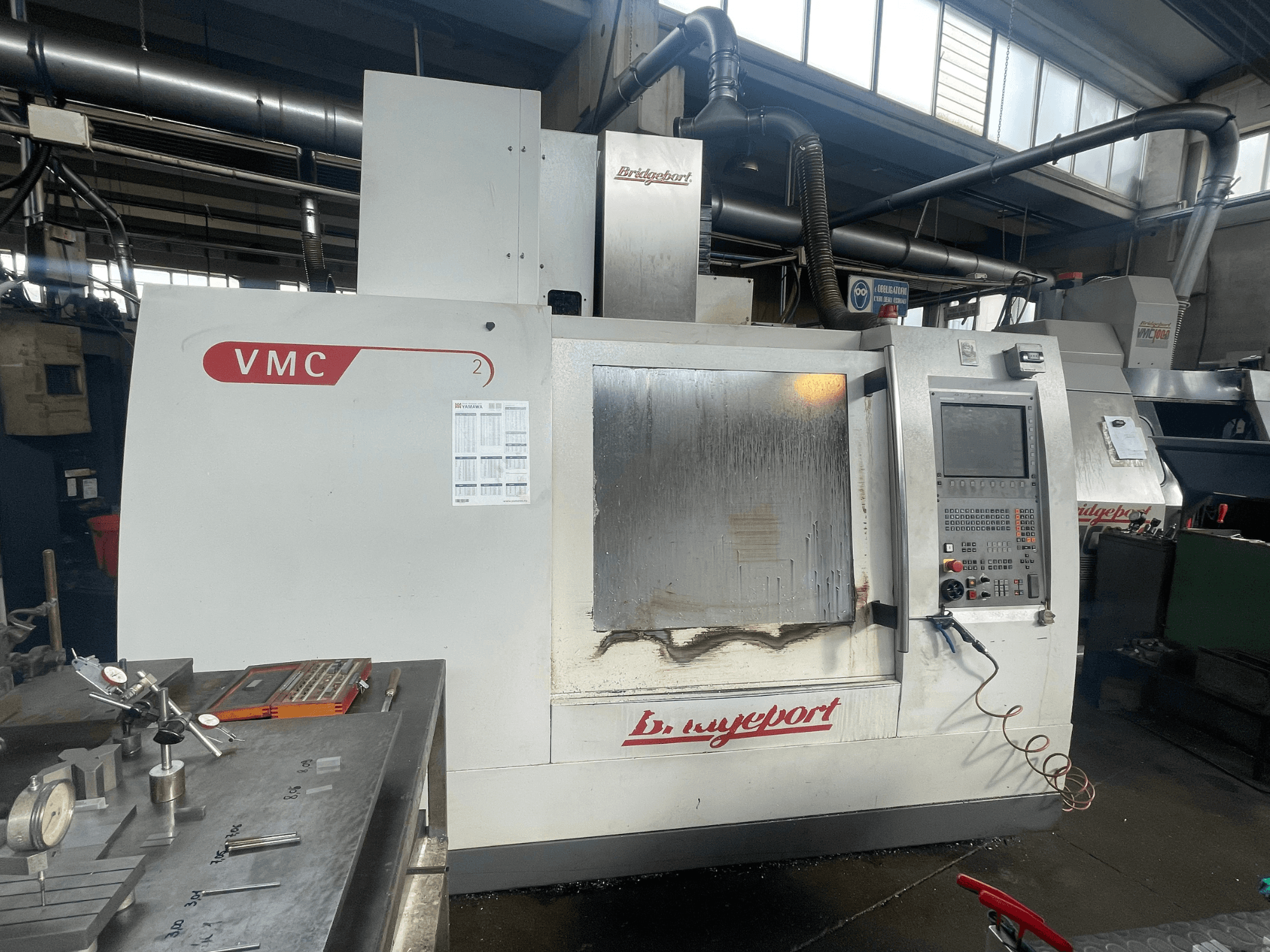Bridgeport VCM 800-30 -pystykoneistuskeskus työpajassa, jossa näkyvät ohjauspaneeli ja työkalupöytä. Etunäkymä, jossa yksityiskohdat ovat selvästi näkyvissä.