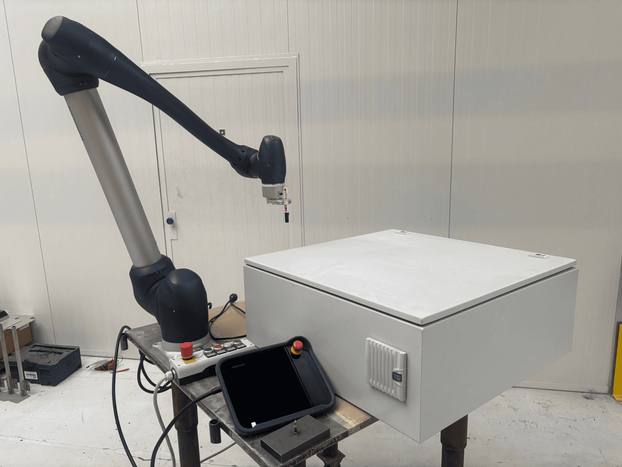 DOOSAN M0617 -yhteistyörobotti sivukuvassa, robottikäsi ojennettuna ohjausliittymän ja pöydällä olevan valkoisen laatikon yläpuolella.