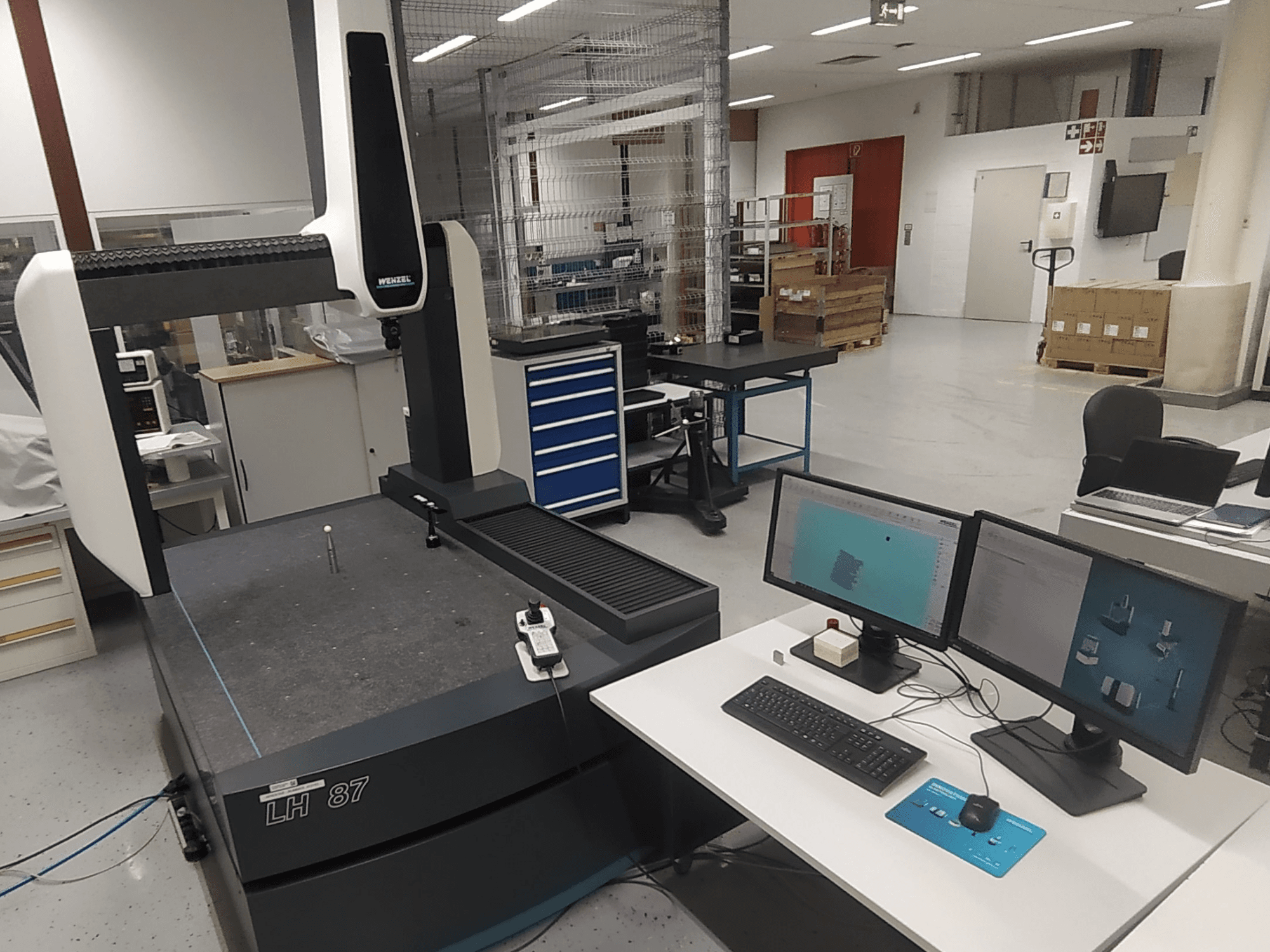 Wenzel LH 87 -koordinaattimittauskone laboratorioympäristössä, jossa on kaksi monitoria ja mittausanturi pöydällä.