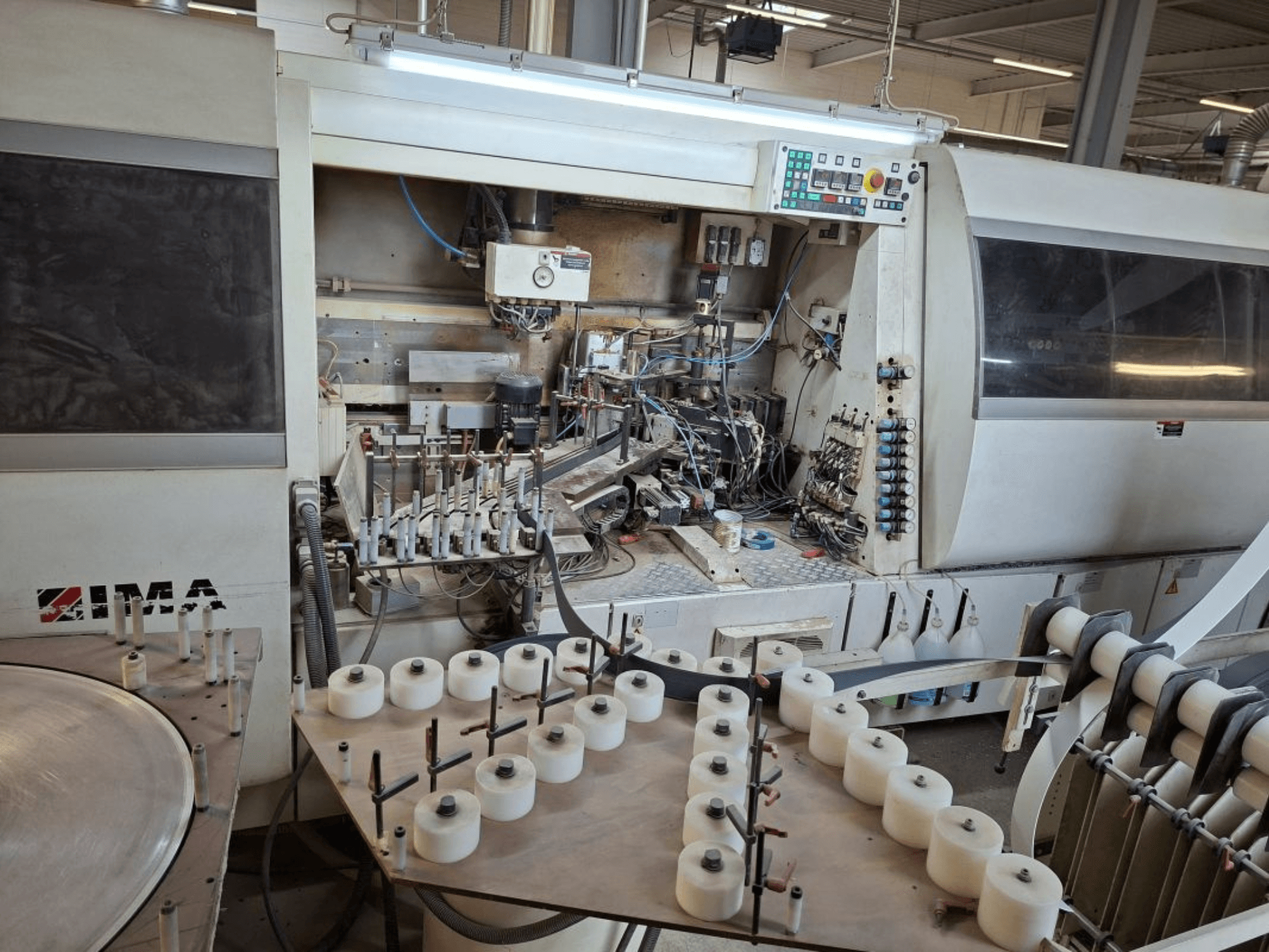 IMA:n koneet sivulta katsottuna, monimutkaiset mekaaniset komponentit ja pyöreä pöytä, jossa on valkoisia keloja.