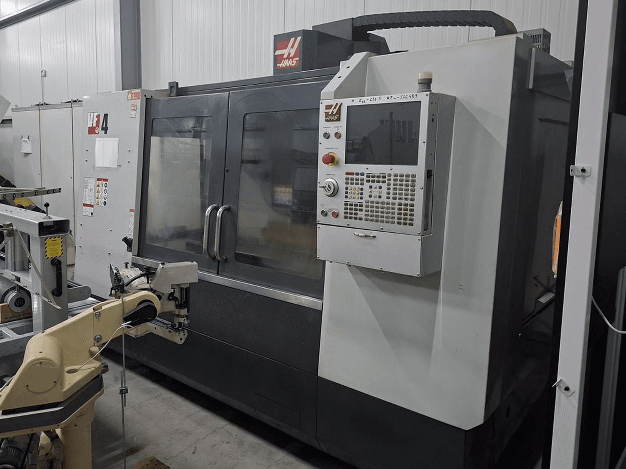 Haas VF-4 CNC-jyrsinkone etukuvassa, jossa on numeerinen ohjauspaneeli ja robottivarsi automaatiota varten.