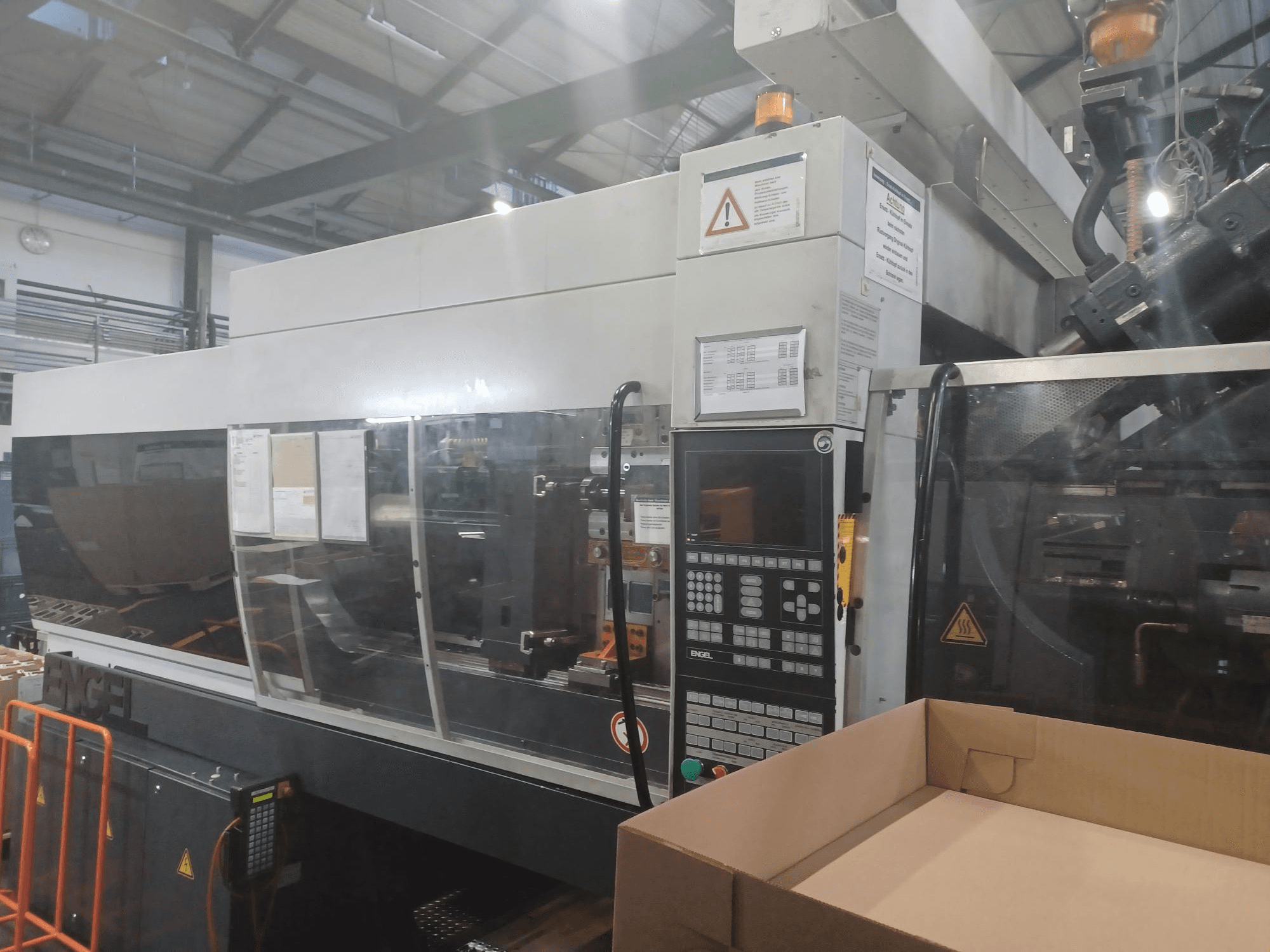 Engelin ruiskuvalukone, etukuva, jossa on ohjauspaneeli, turvatarrat ja tyhjä laatikko lähellä.