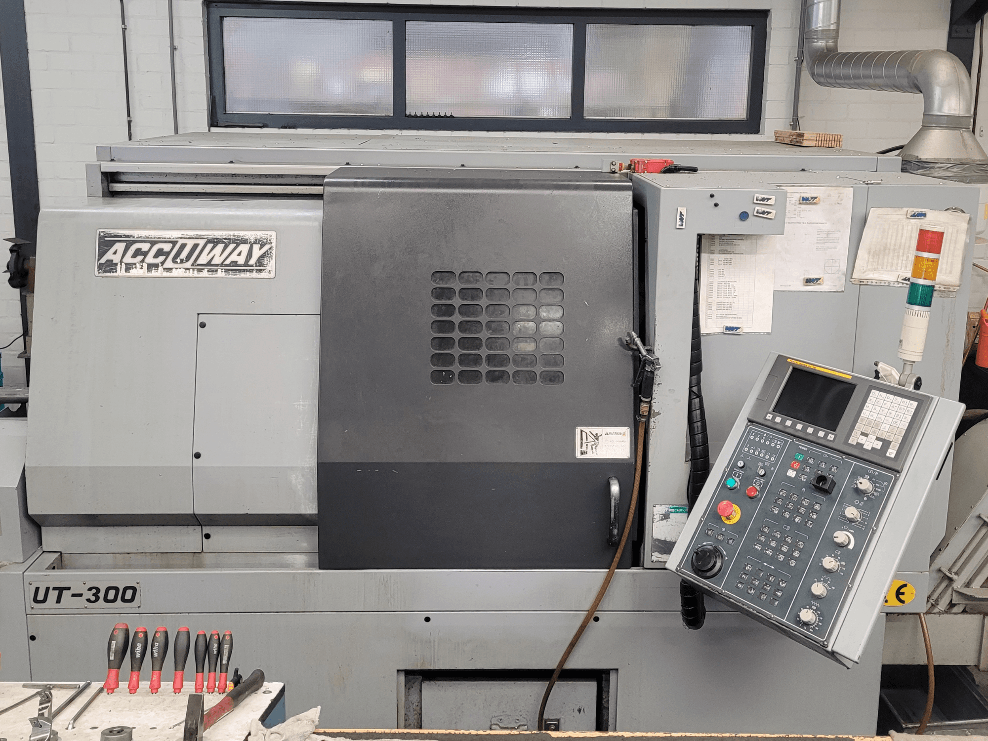 Accuway UT-300 CNC-kone edestä katsottuna, jossa on ohjauspaneeli ja erilaisia käyttöpainikkeita, työpajassa.