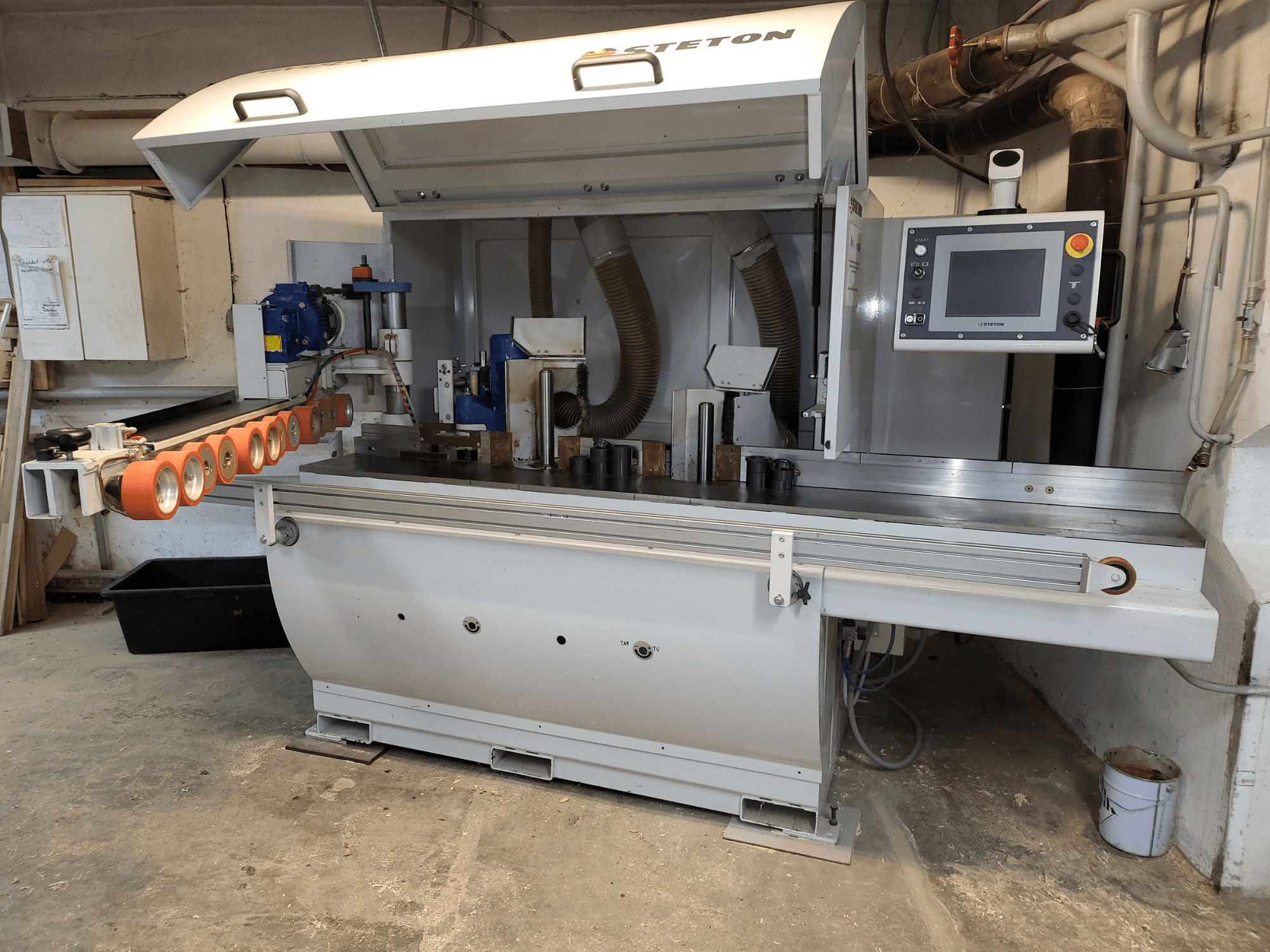 Etukuva Stetton-puuntyöstökoneesta, jossa on ohjauspaneeli, syöttöputket ja erilaisia puukappaleita pöydällä.