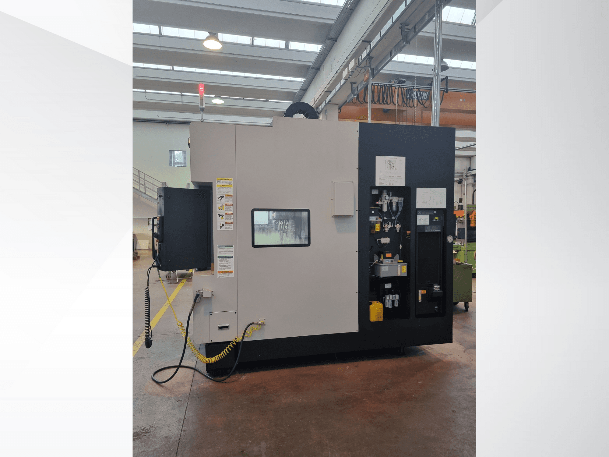 Teollisuuskone sivukuvassa, jossa on ohjauspaneeli, jossa on painikkeita, merkkivaloja ja turvallisuusvaroitustarra.