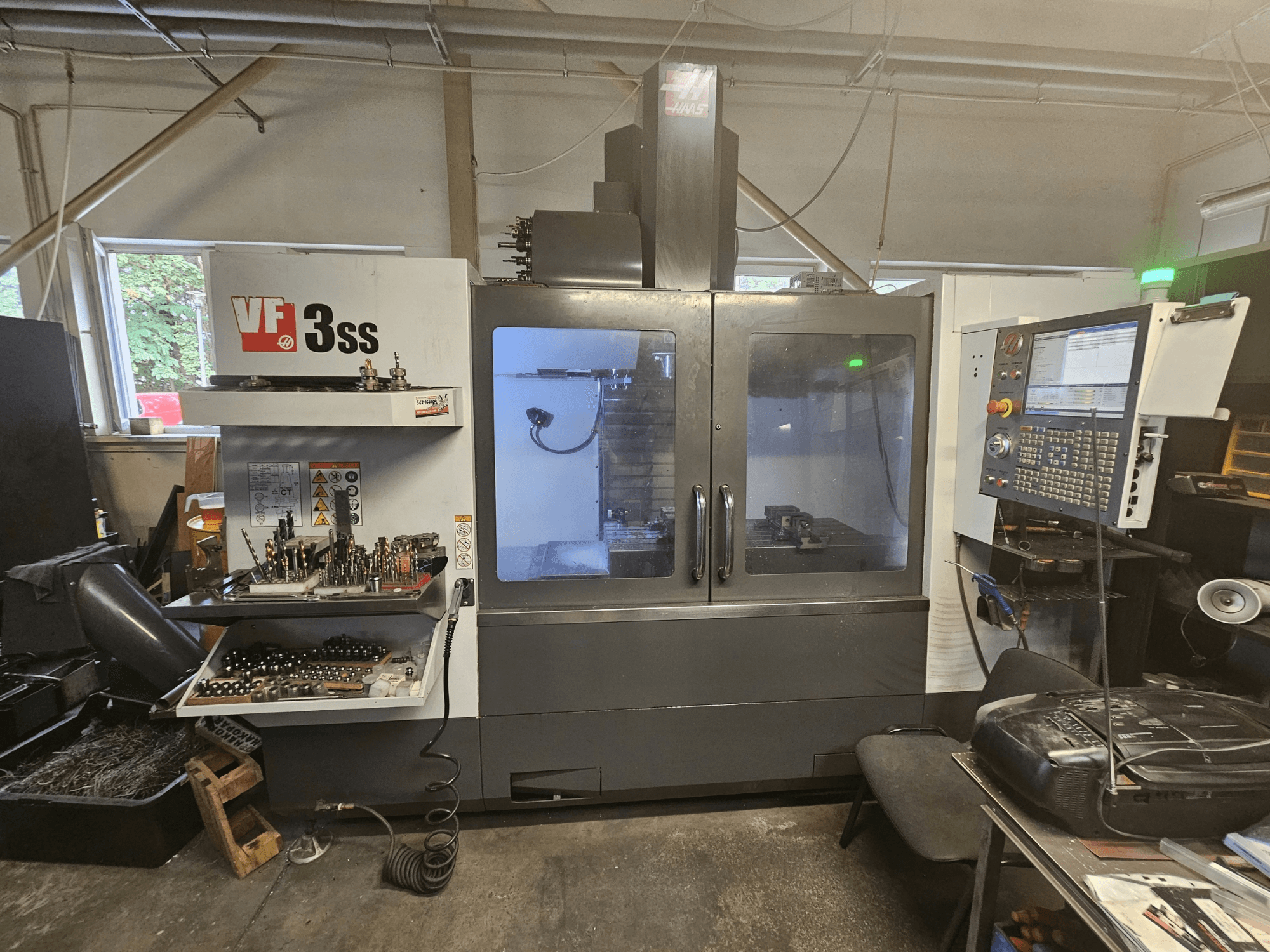 Haas VF-3SS -pystykoneistuskeskus työpajassa, etunäkymä, jossa näkyvät ohjauspaneeli ja työkalujen säilytyslokero.