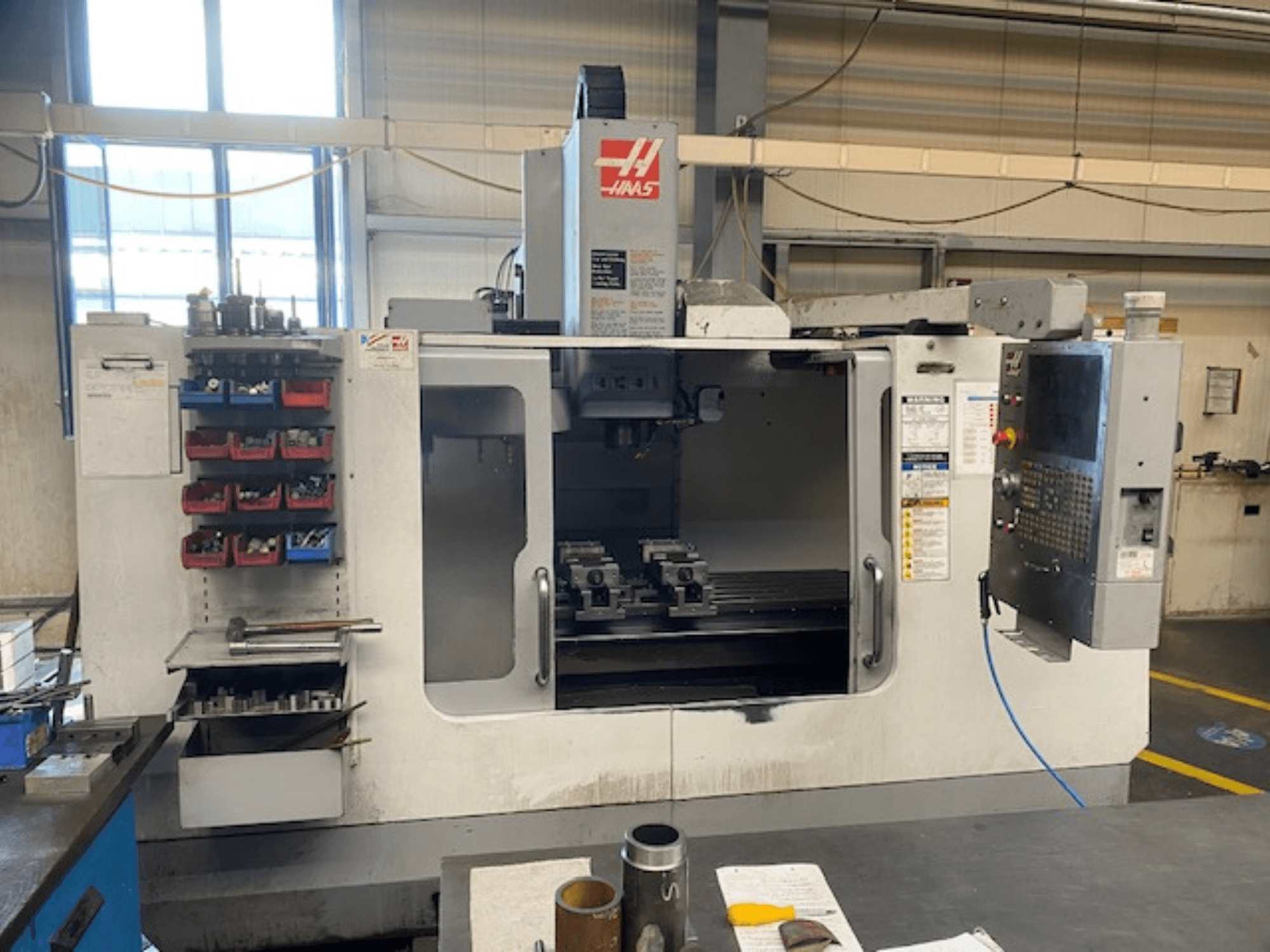 Haas CNC-jyrsinkoneen etukuva, malli VF-2, jossa työkalujen säilytys, ohjauspaneeli ja työtilan työkalut näkyvissä.