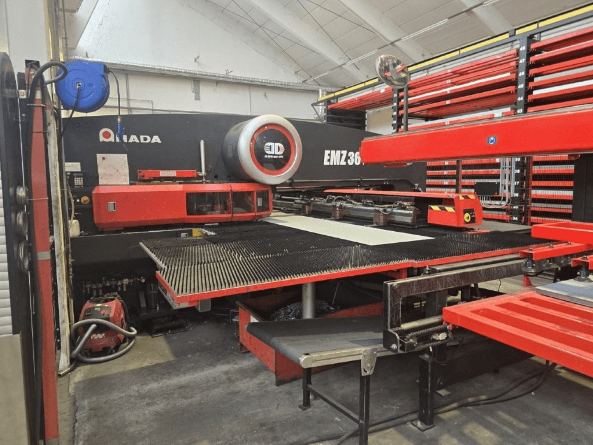 Amada EMZ 36 -laserleikkauskone työpajassa, etukuva, punaiset korostukset ja suuri leikkauspöytä.
