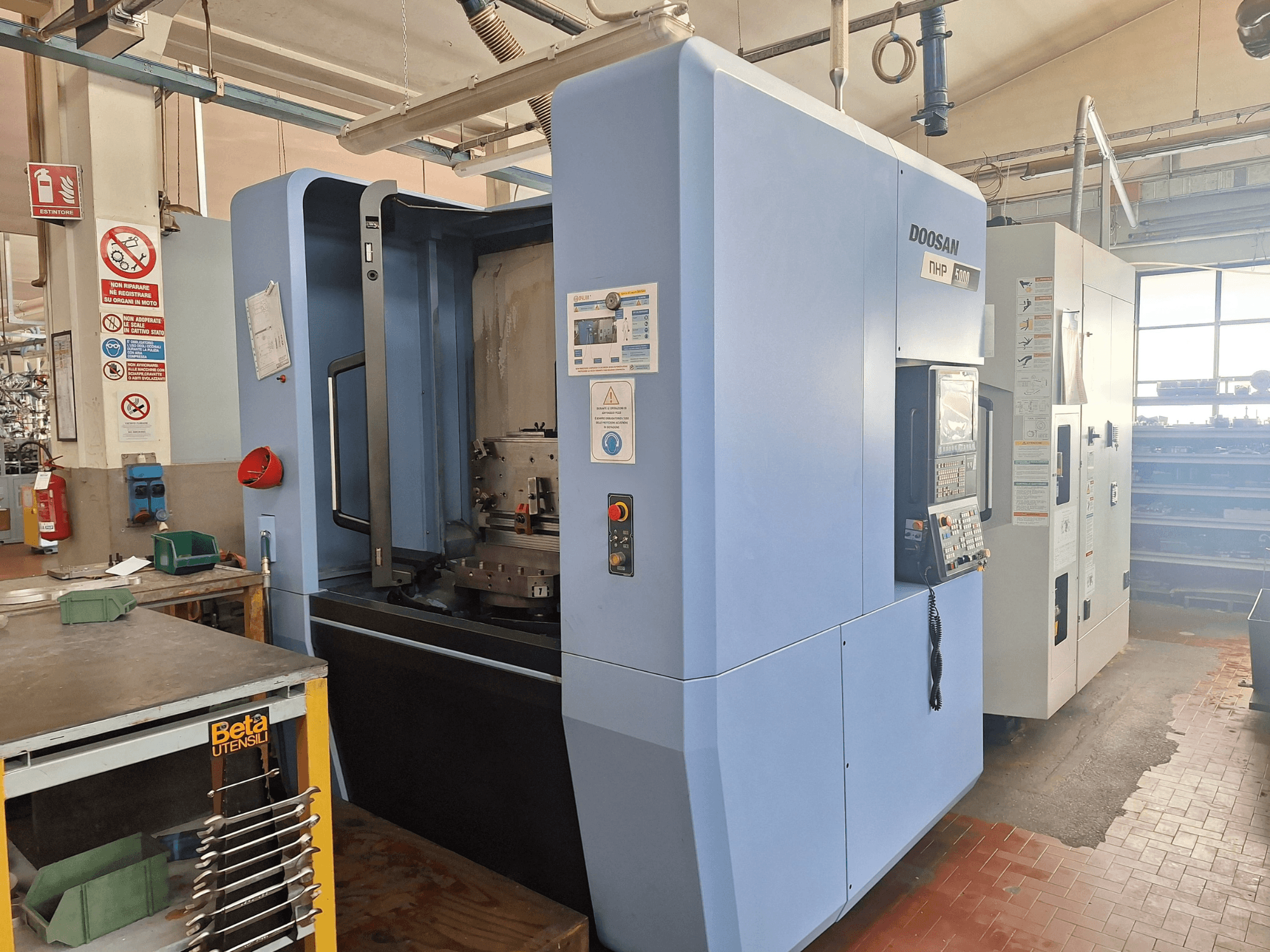 DOOSAN NHP 5000 -vaakakoneistuskeskus työpajassa, sivukuva, jossa näkyy sen ohjauspaneeli ja koneistusalue.