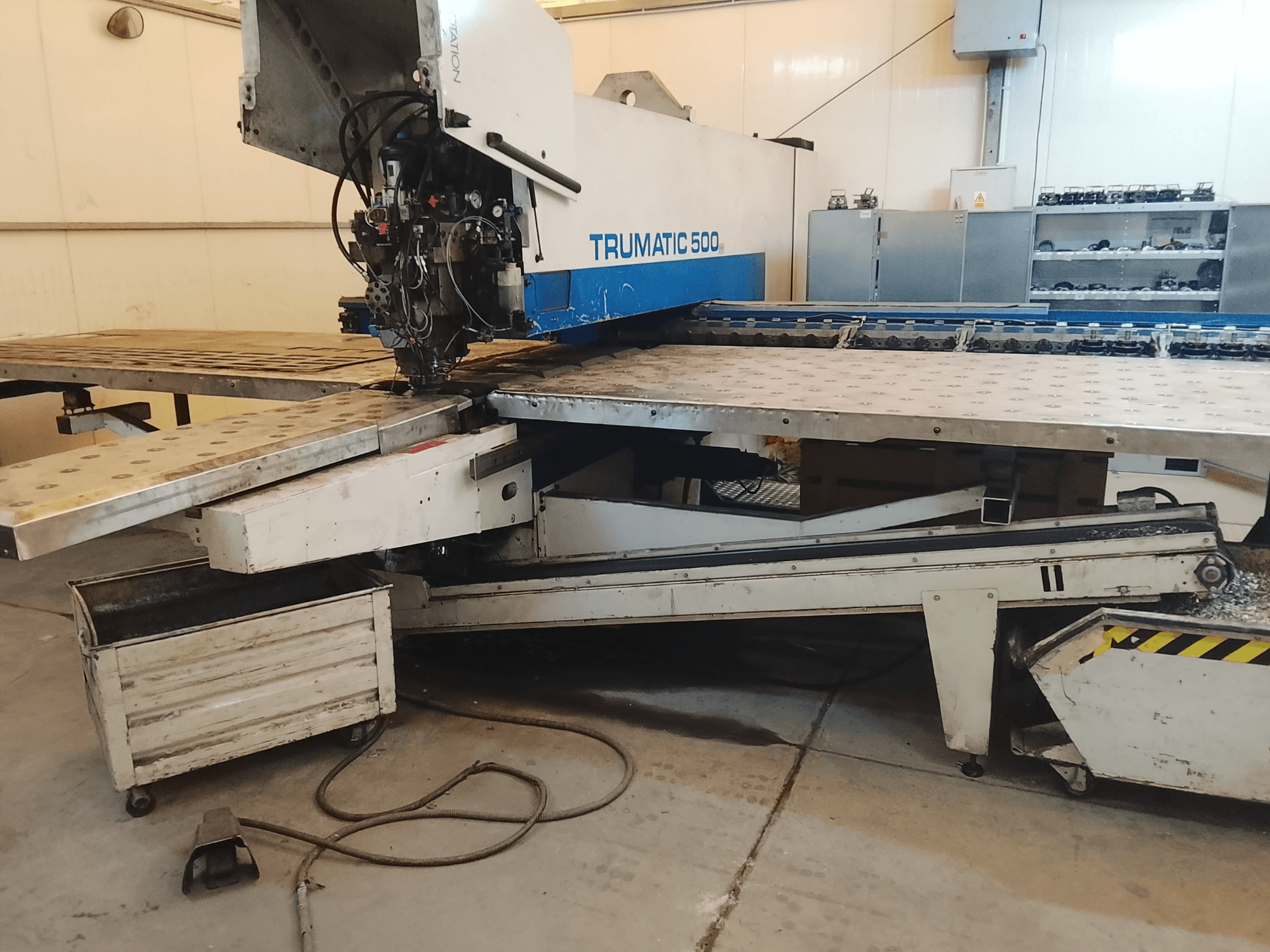 TRUMATIC 500 CNC-kone työpajassa, sivukuva, jossa näkyy leikkuupää ja metallityöpöytä, jossa on esiporattuja reikiä.
