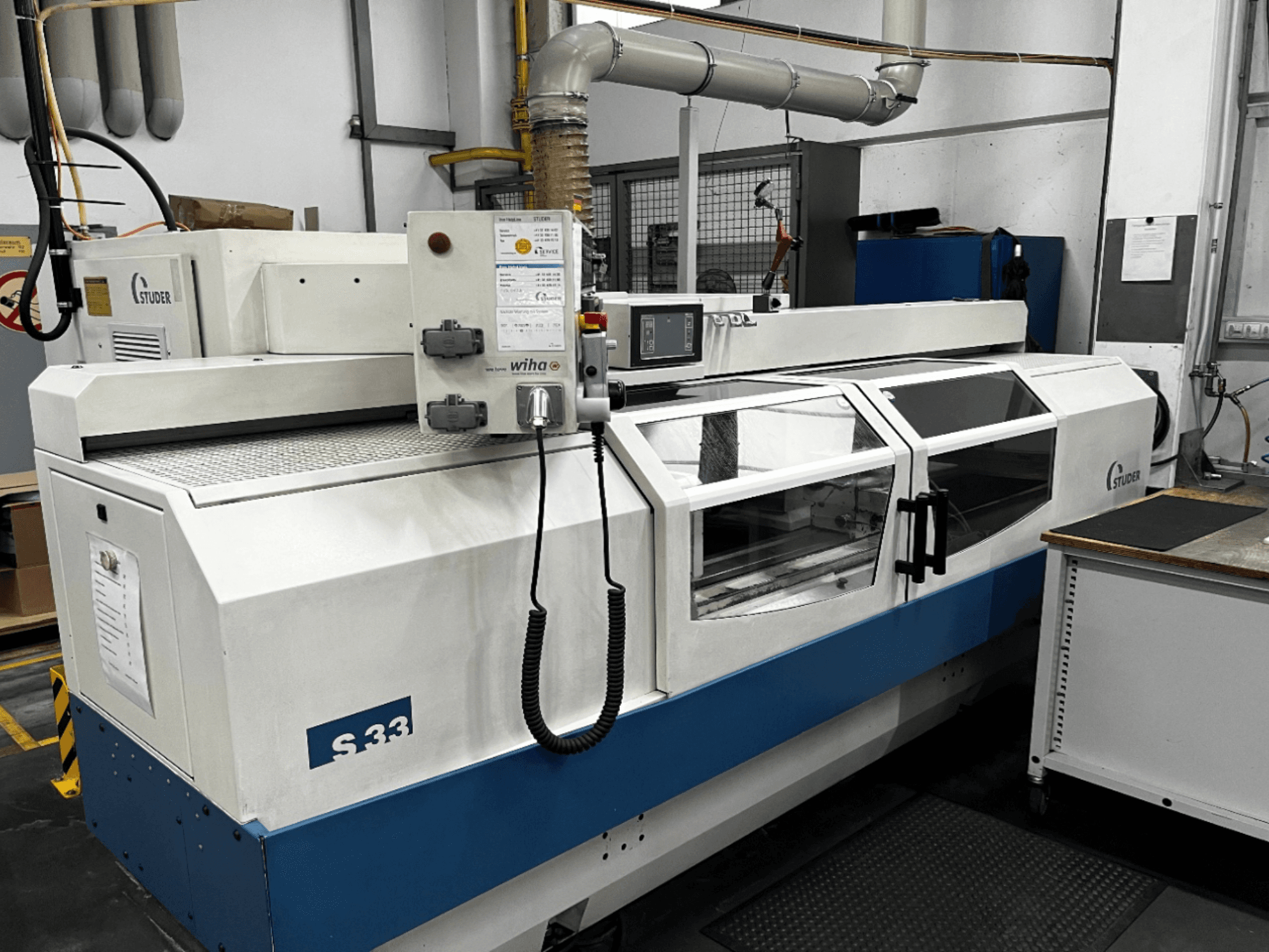 STUDER S33 CNC-sylinterihiomakone, etukuva; ohjauspaneeli ja lasiset turvaovet. Teollisuusympäristö.