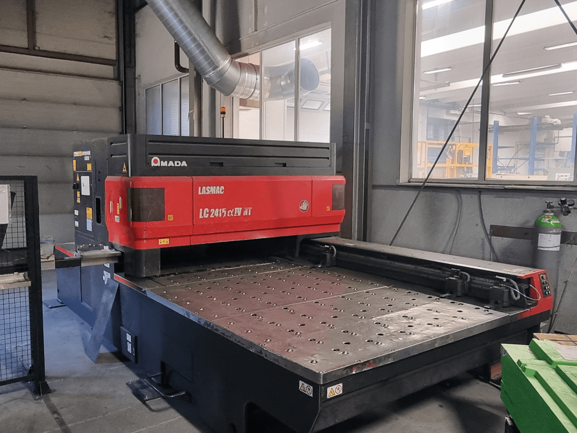 Amada LASMAC LC 2415 αⅡ NT -laserleikkauskone, punainen ja musta, etukuva, jossa on sähkökäyttöinen leikkuupeti ja tarkkuusohjaus.