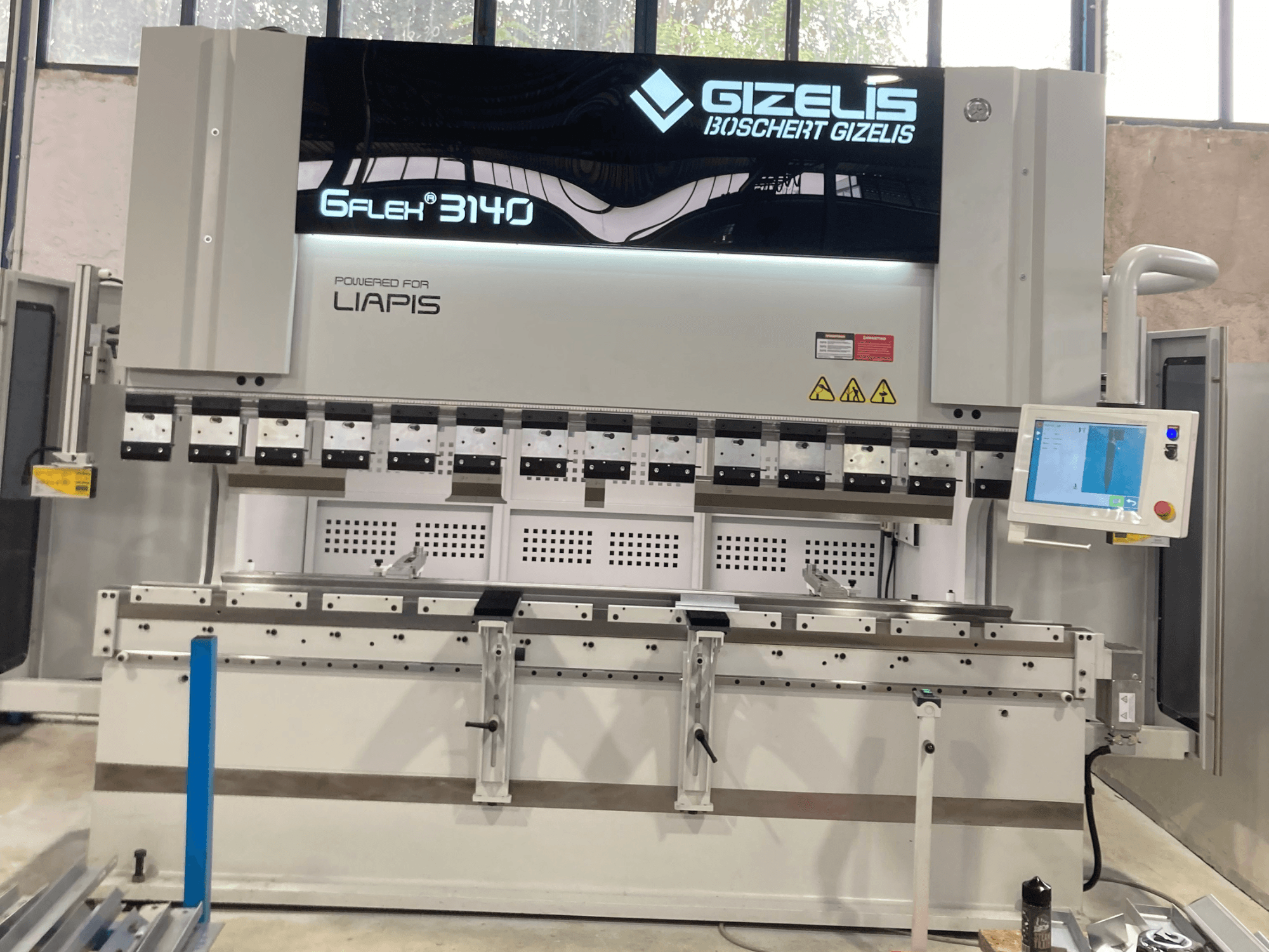 Hydraulinen puristin GIZELIS G-FLEX 3140 edestä katsottuna ohjausnäytöllä, jossa on useita taivutustyökaluja ja turvatarrat.