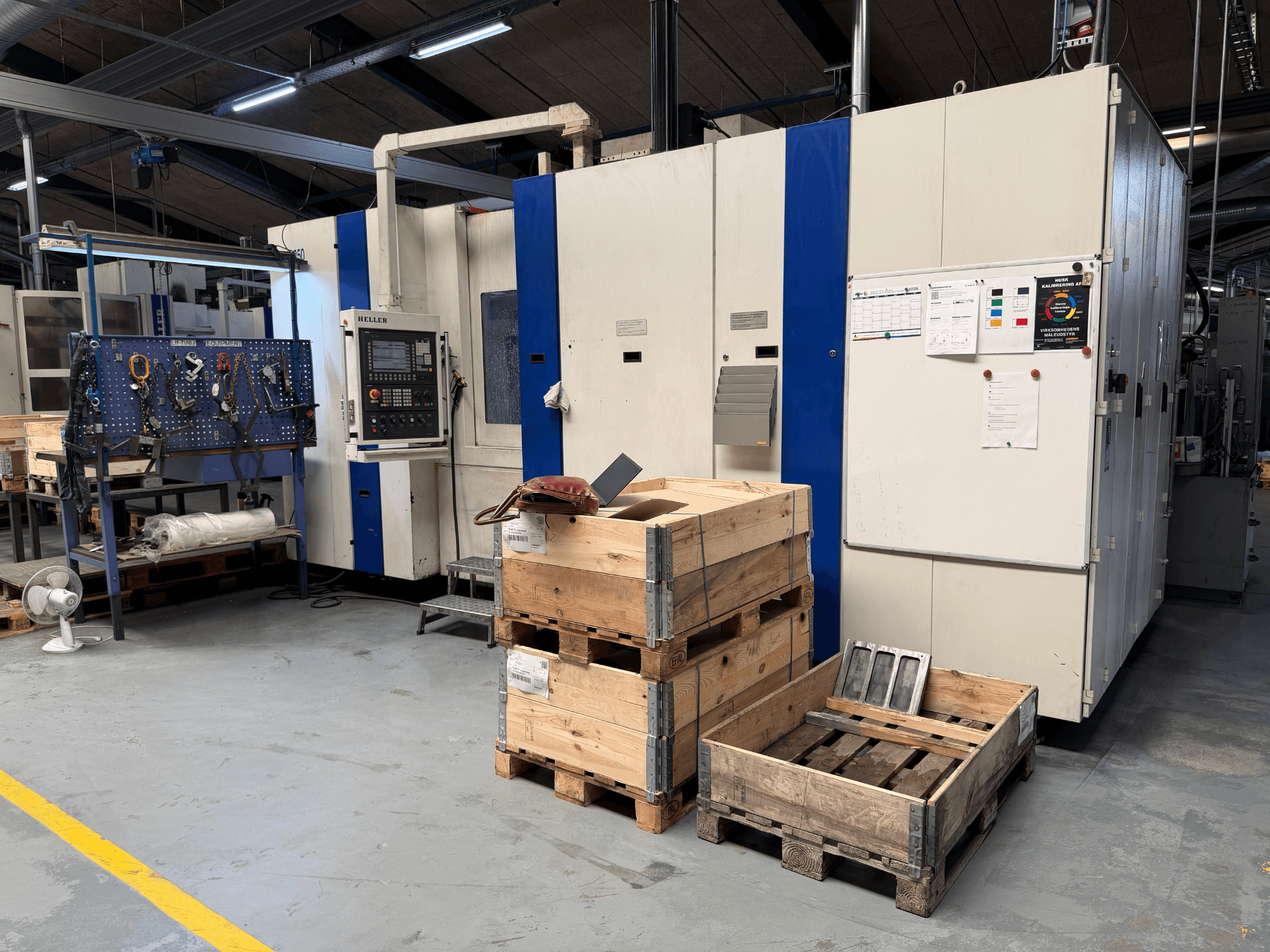 HORIZONTAL MACHINING CENTRE HELLER MCH 250 työpajassa, sivukuva, jossa puiset kuormalavat ja työkaluhylly näkyvissä.