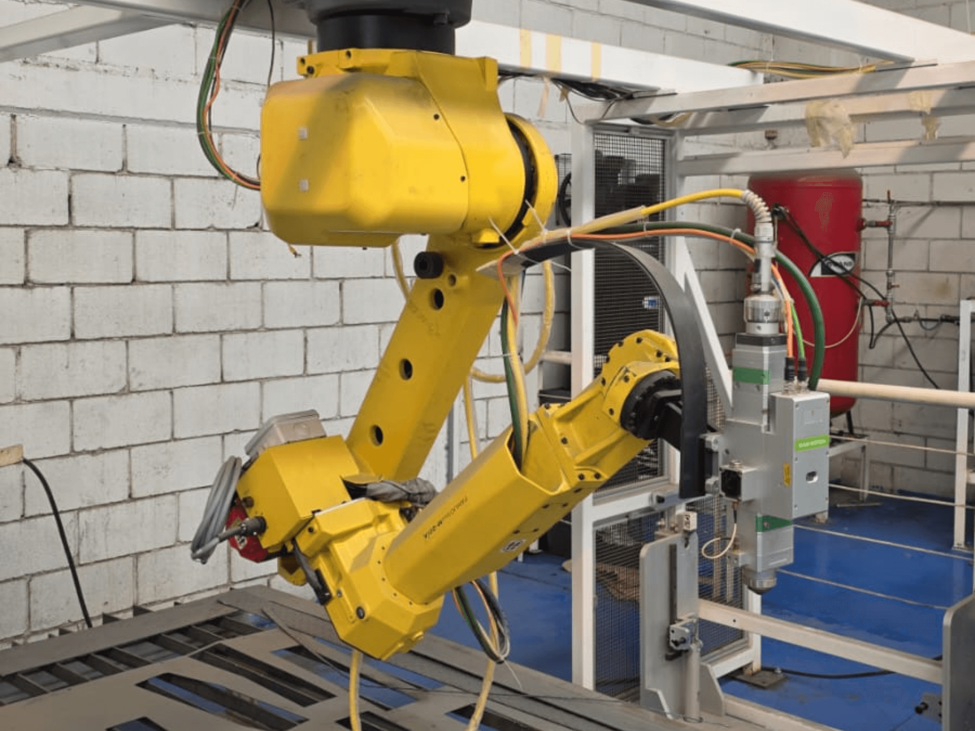 Keltainen robottikäsivarsi, jossa on tarkkuustyökalu, jossa on useita niveliä ja kaapeleita, etukulmasta katsottuna teollisuusympäristössä.