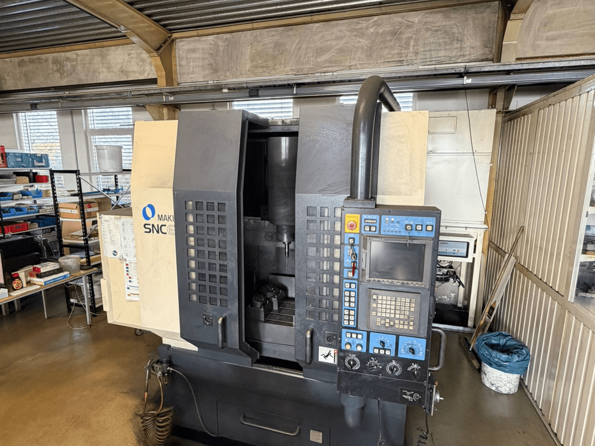 Makino SNC 64-A15 -pystytyöstökeskus edestäpäin, jossa näkyy ohjauspaneeli, työstöalue ja teollinen työtila.