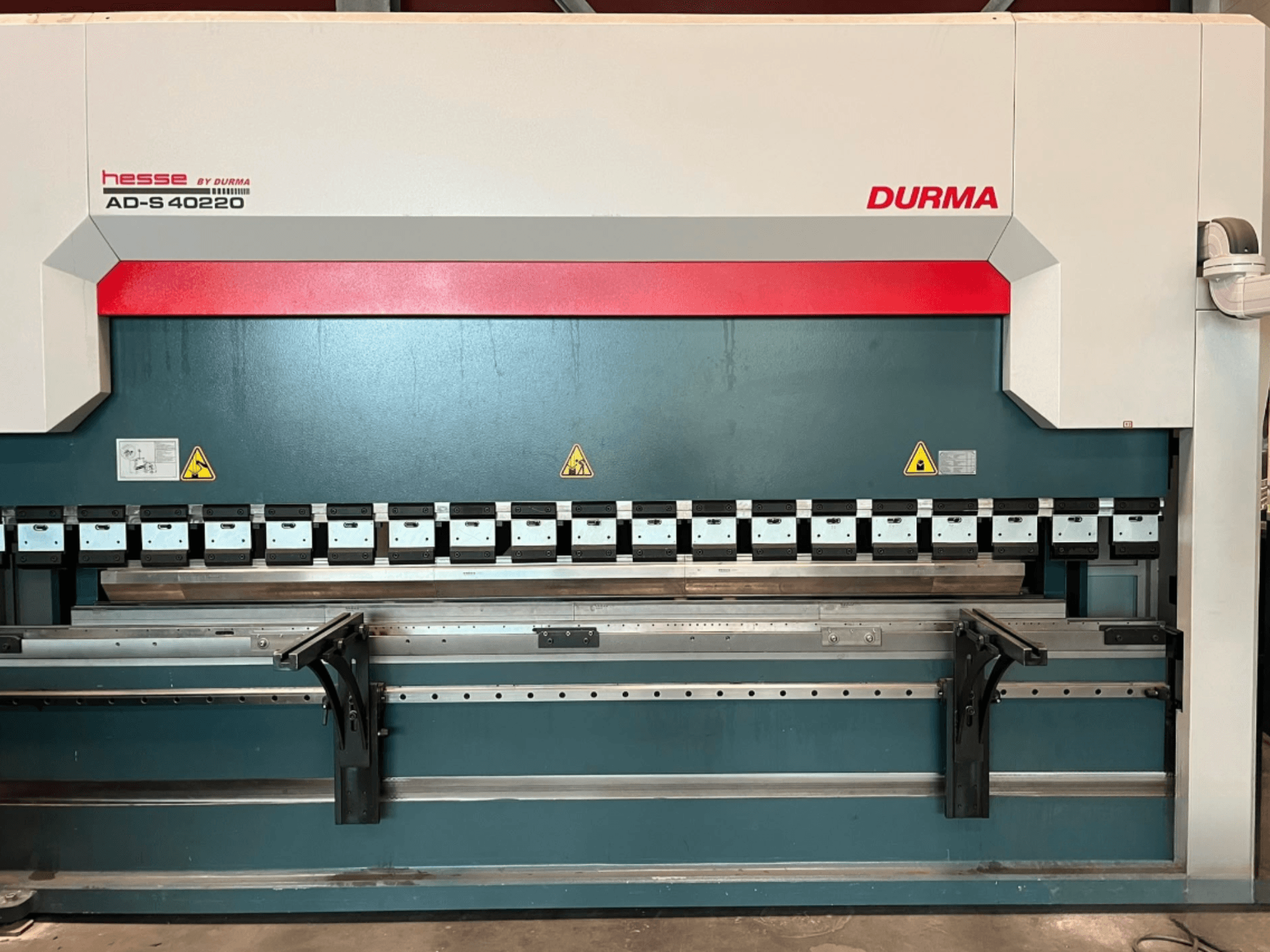 Durma AD-S 40220 -taivutuskone edestä katsottuna, jossa on useita taivutustyökaluja ja turvallisuusmerkintöjä.
