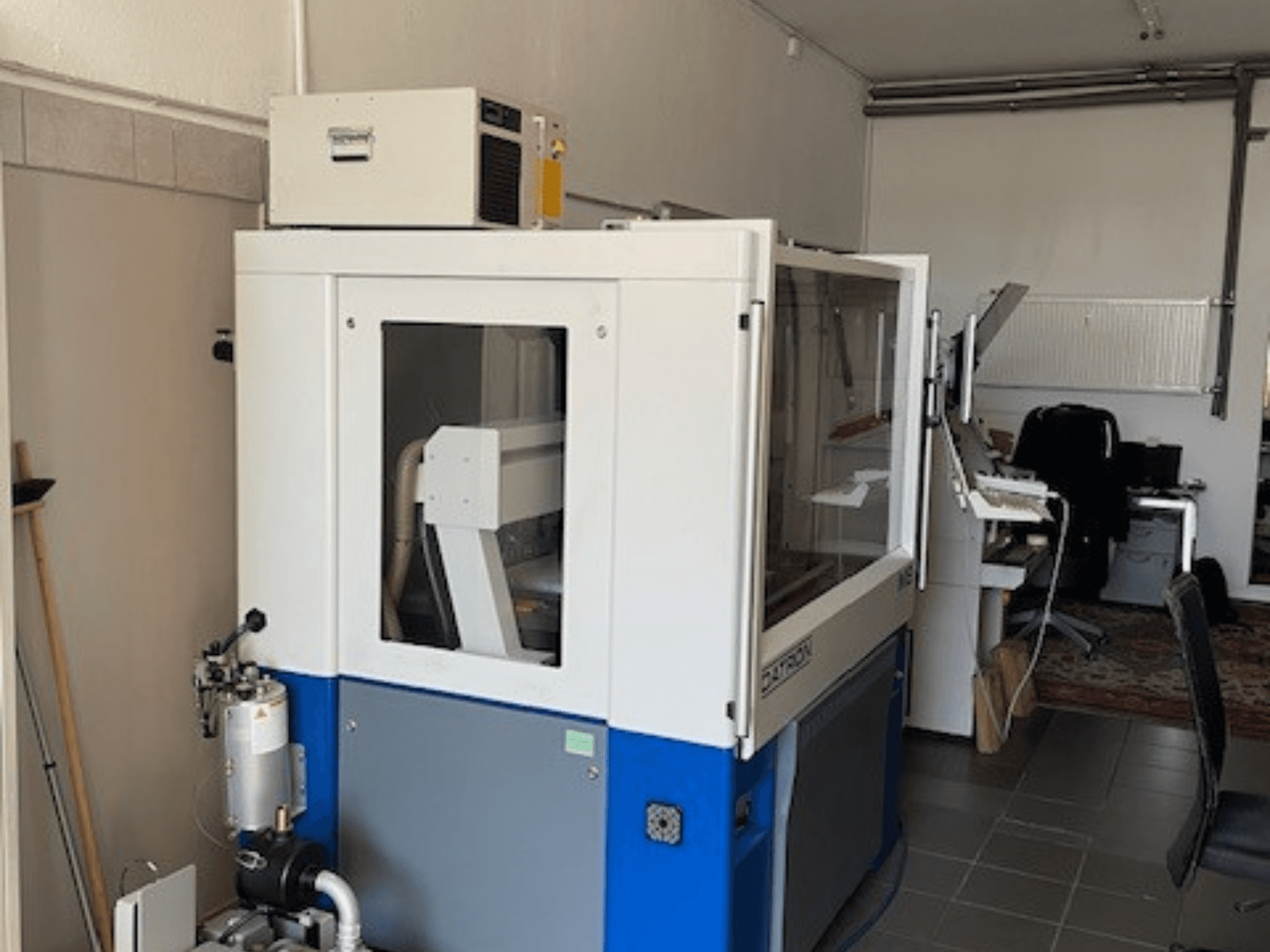 Sinivalkoinen teollisuuskone, jossa on läpinäkyvät paneelit, etukuva, sisältää ohjausyhteyden ja näkyvän ilmanvaihtoyksikön.